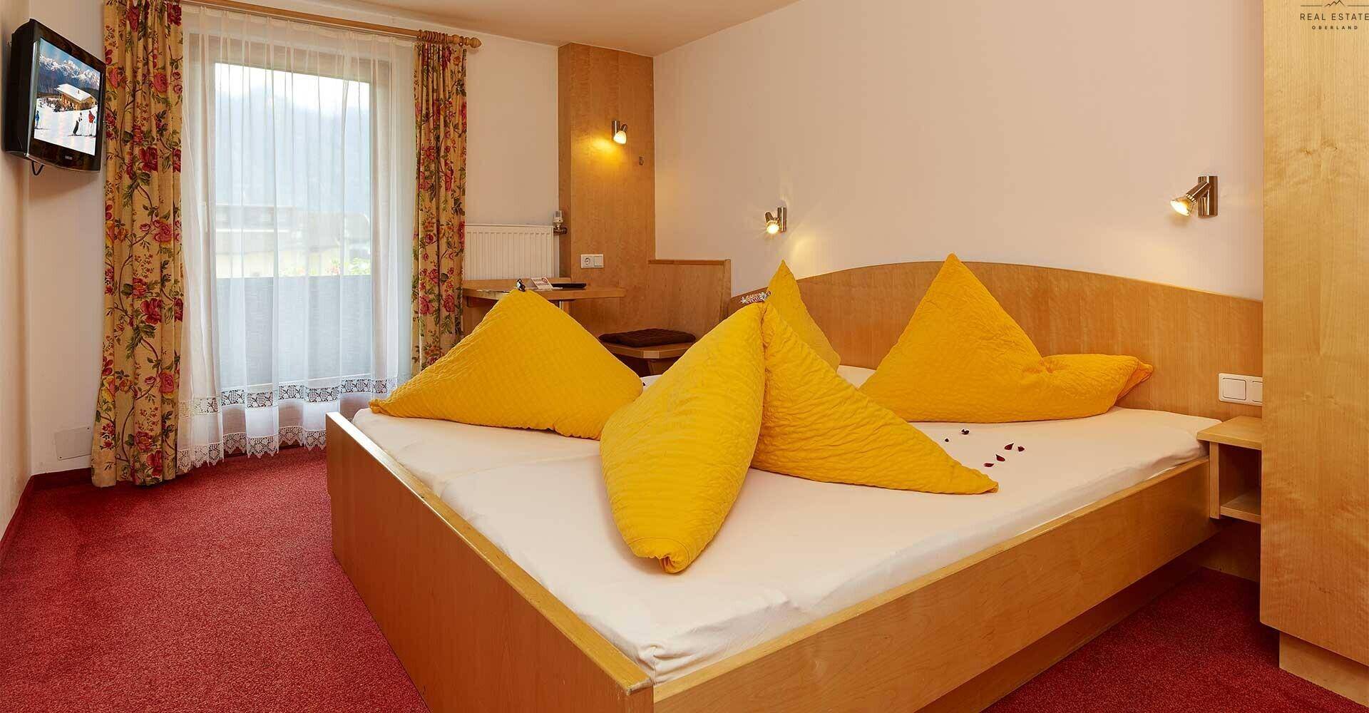 Schlafzimmer mit Doppelbett, gelber Bettwäsche und Zugang zu einem Balkon mit Bergblick.