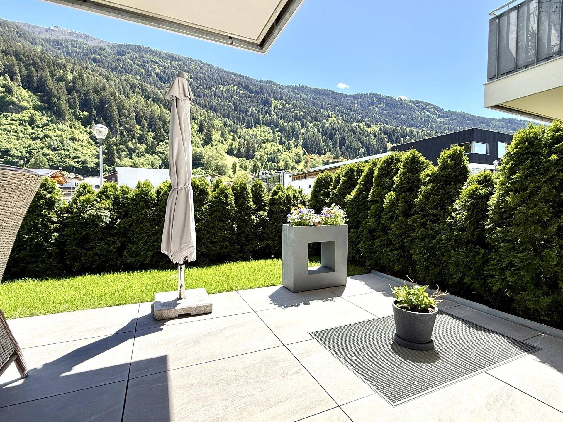 Sonniger Terrassenbereich mit Gartenmöbeln, Sonnenschirm und beeindruckendem Bergblick.