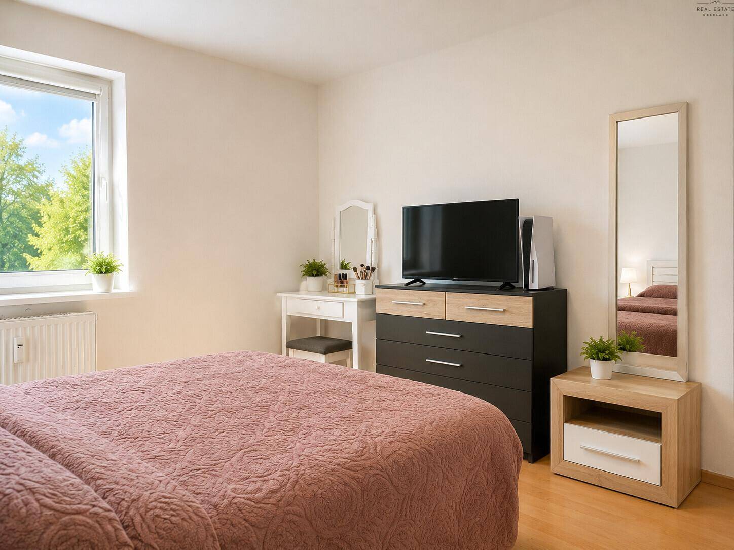 Schlafzimmer mit Doppelbett, Kommode, Fernseher und hellem Fenster.