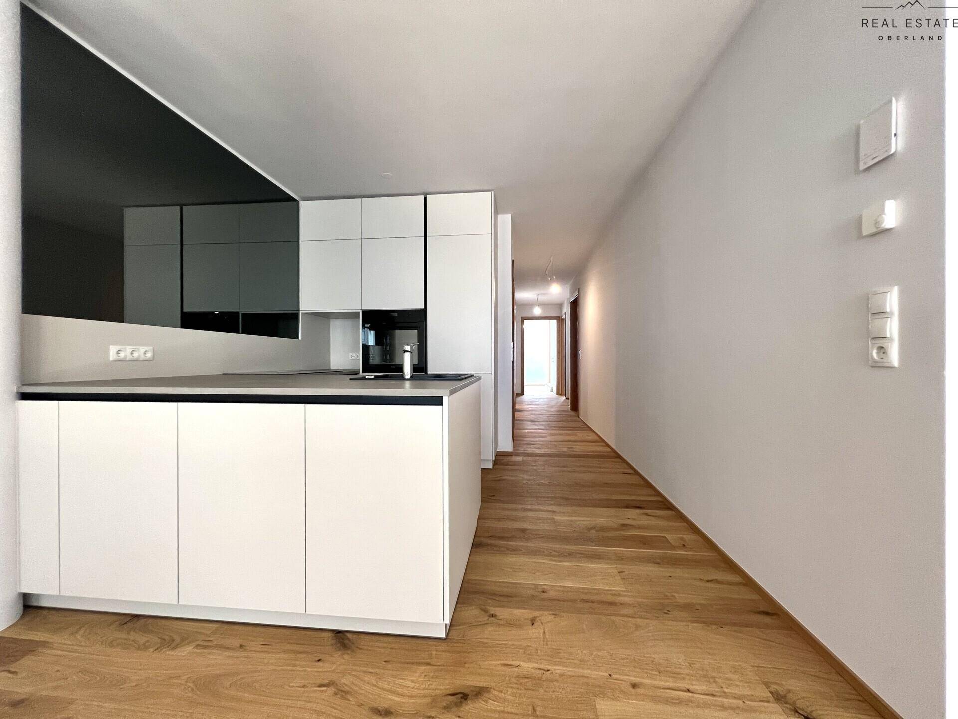 Moderne weiße Einbauküche mit dunkler Arbeitsplatte und integrierten Geräten in offenem Grundriss.
