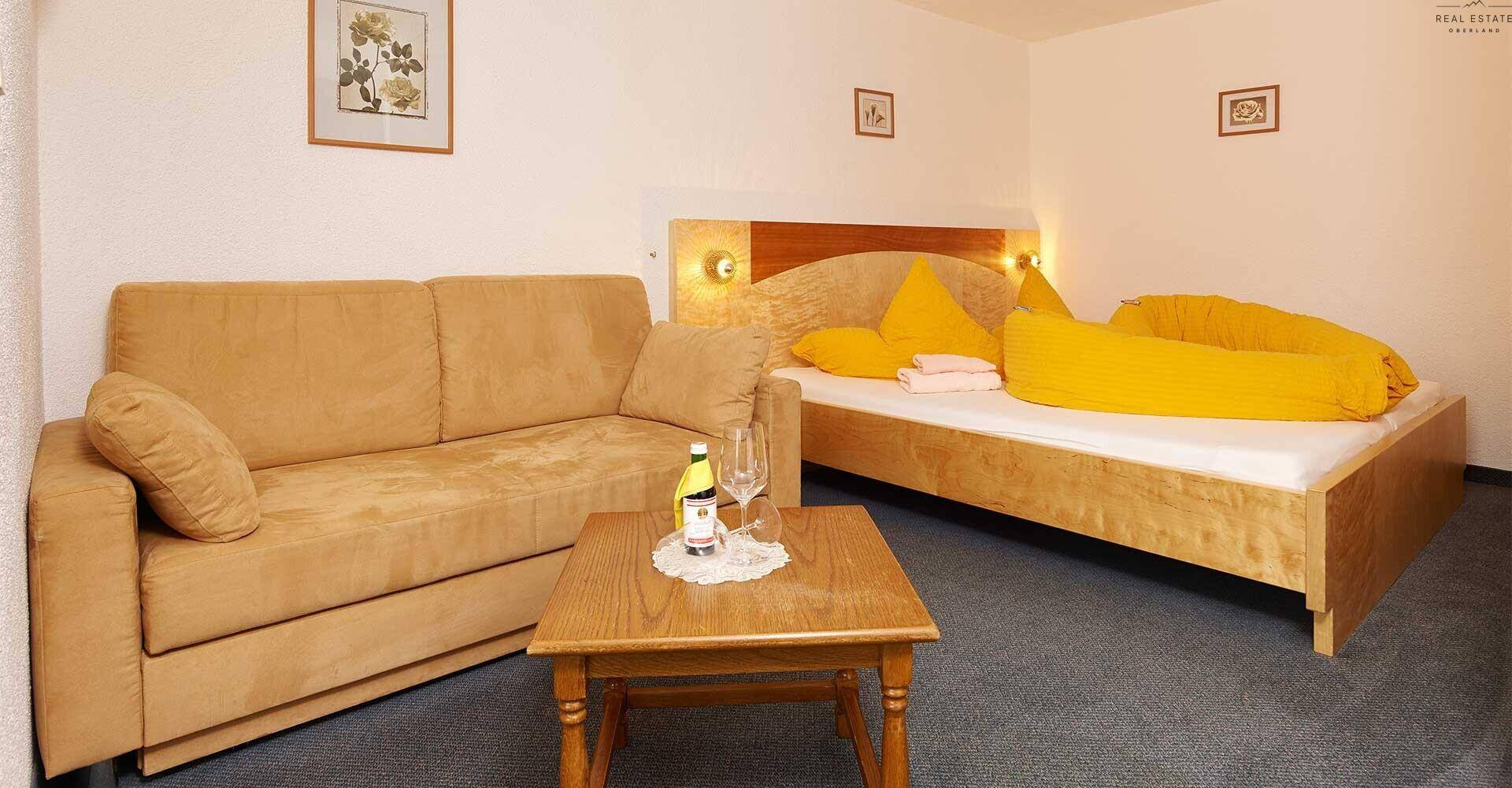 Schlafzimmer mit Doppelbett, beigem Sofa und Couchtisch, in einem gemütlichen Ambiente.