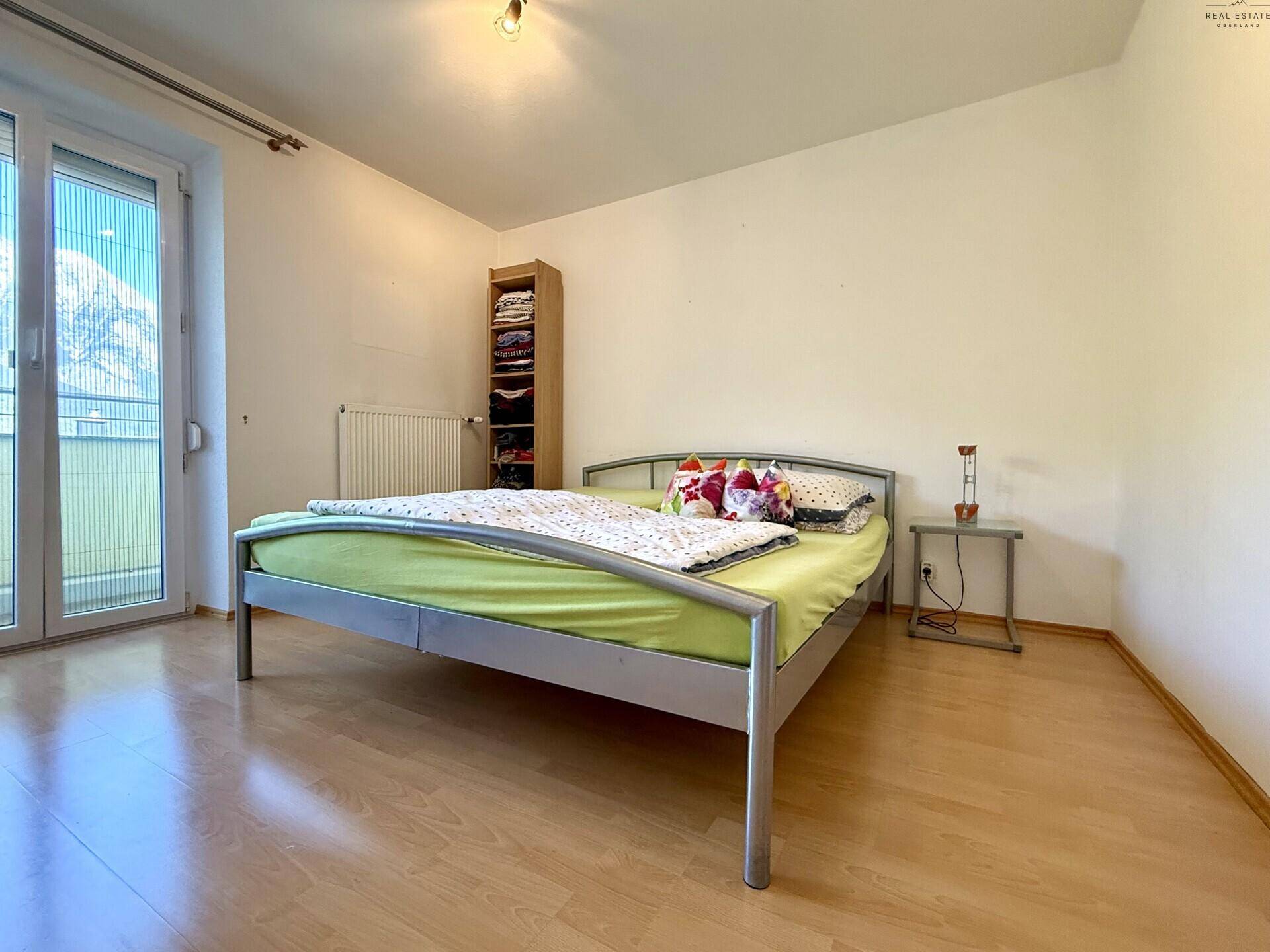 Schlafzimmer mit Metallbett, Laminatboden und Zugang zu einem französischen Balkon.
