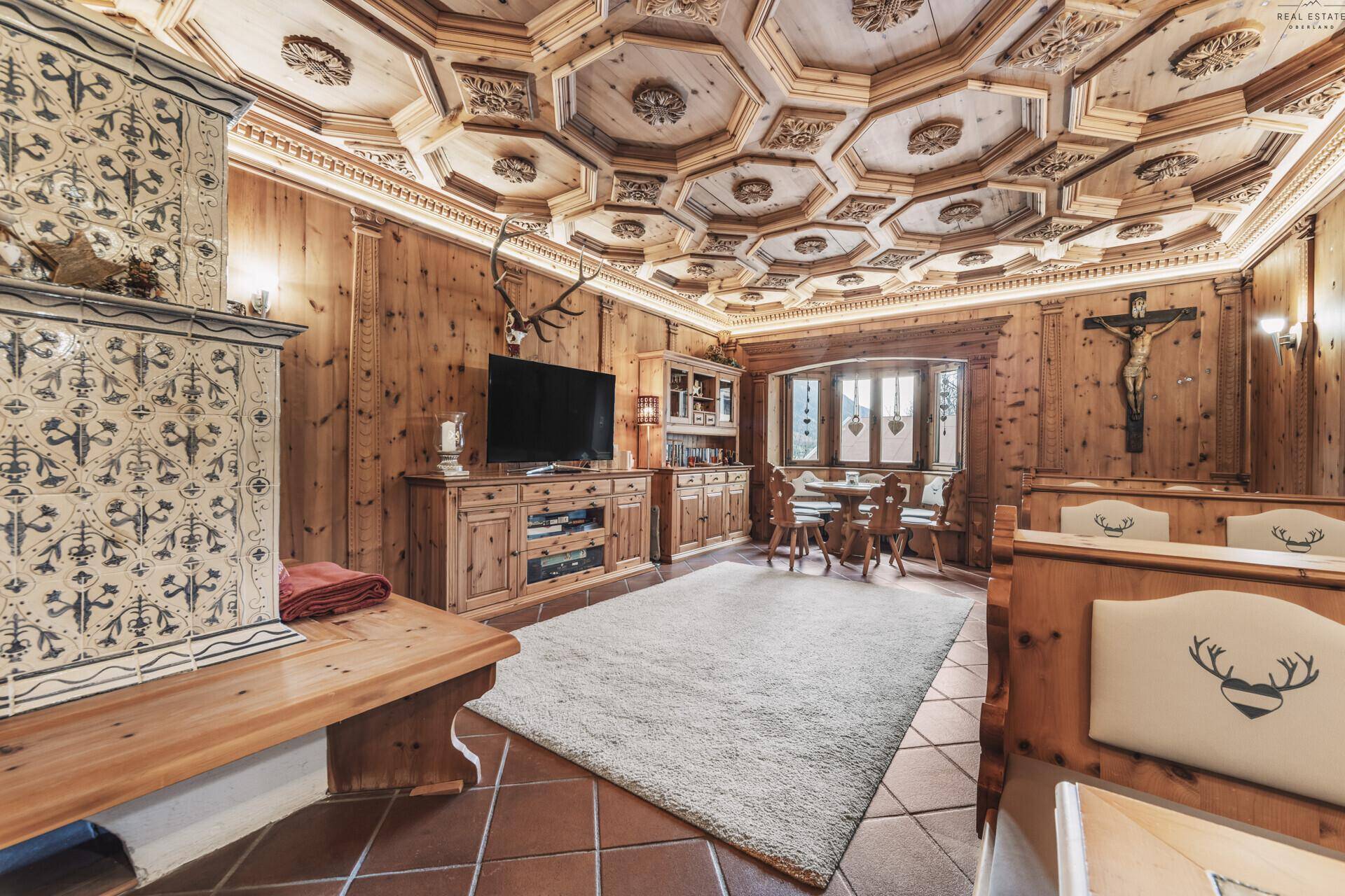 Traditioneller alpiner Wohn- und Essbereich mit Holztischen, Bänken und kunstvoll geschnitzter Decke.