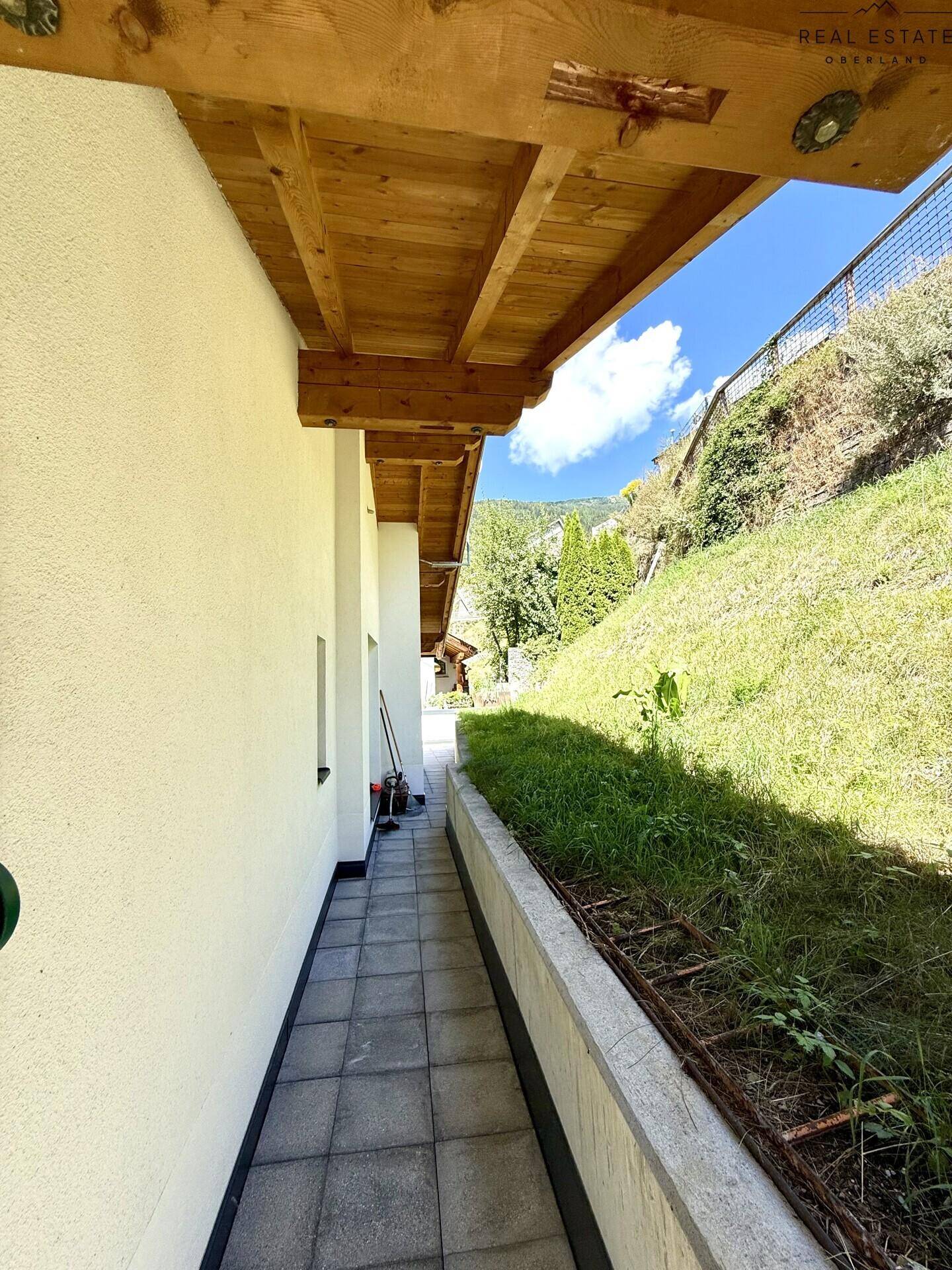 Seitlicher Zugang zum Haus mit gefliestem Pfad und natürlicher Hangbegrünung.