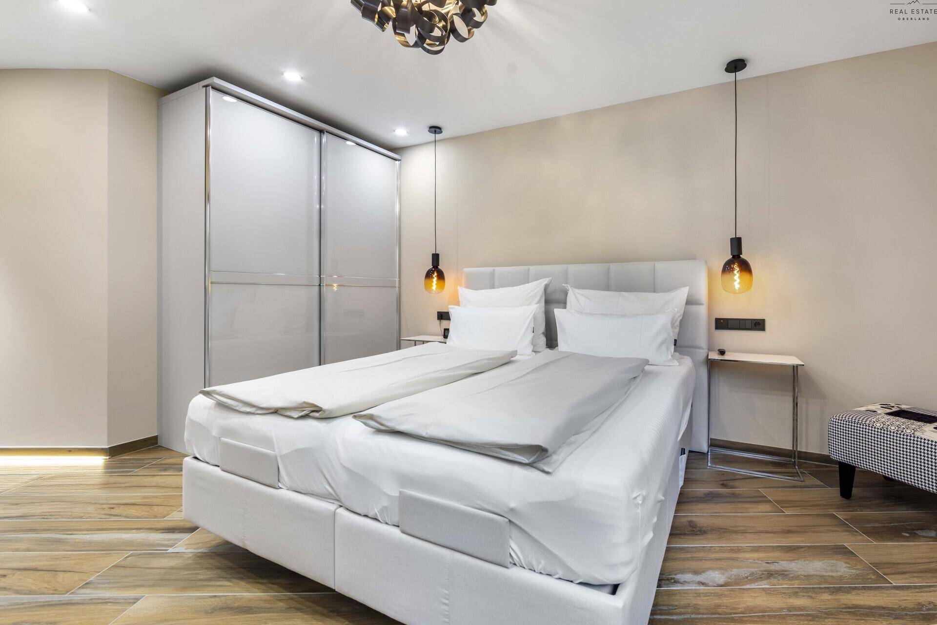 Helles Schlafzimmer mit großem Doppelbett, modernen Pendelleuchten und glänzenden Einbauschränken.