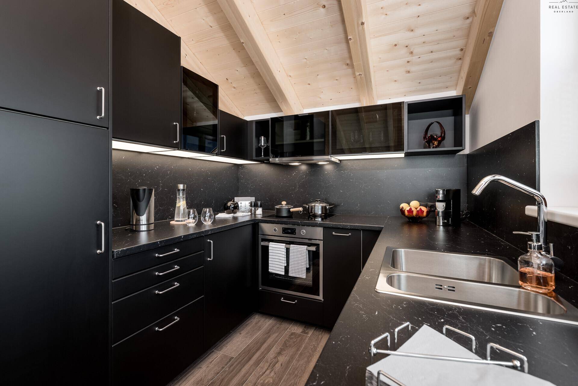 Moderne schwarze Küche mit integrierten Geräten, viel Stauraum und Holzbalkendecke.