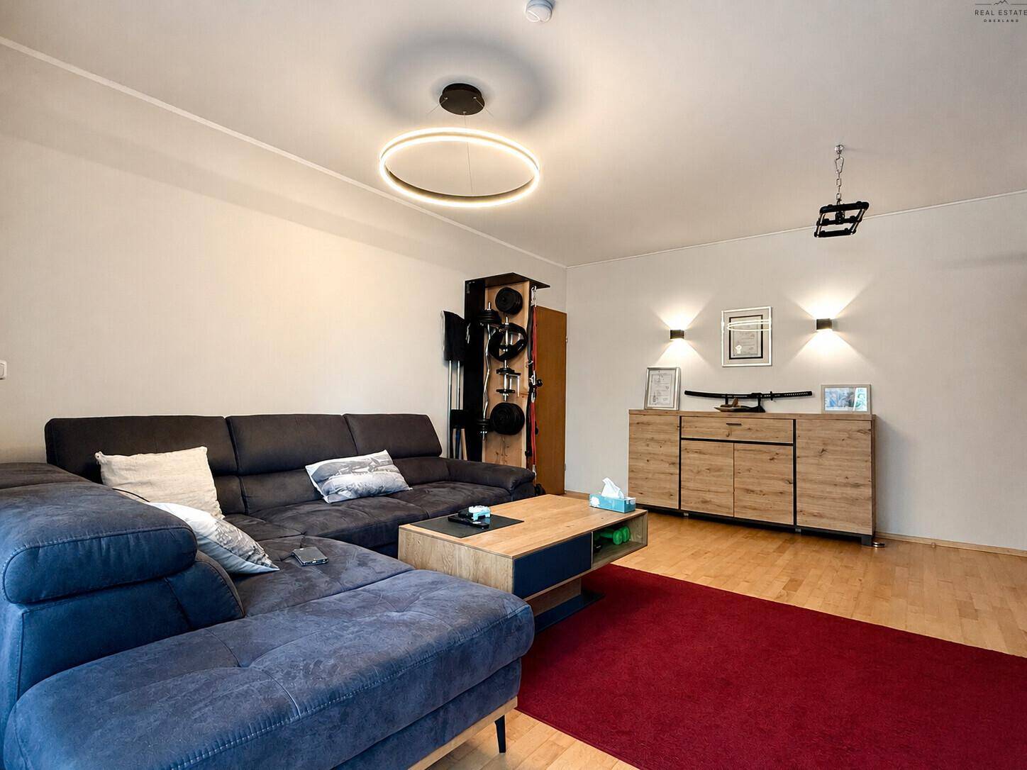 Gemütliches Wohnzimmer mit großem Sofa, Holzboden und moderner Beleuchtung.