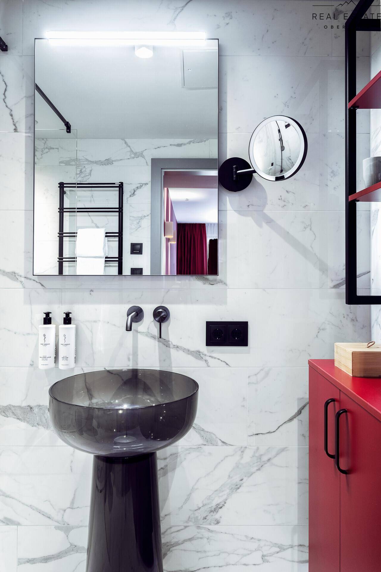 Modernes Badezimmer mit Marmorfliesen, schwarzem Waschbecken und beleuchtetem Spiegel.