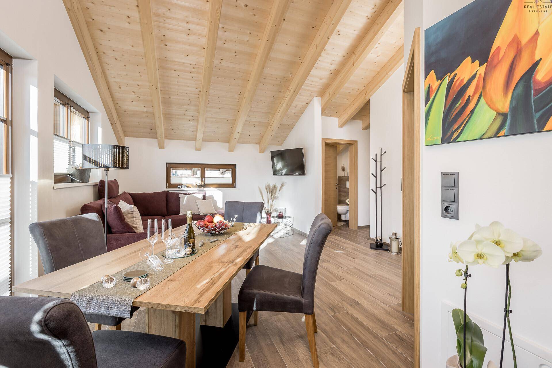 Geräumiger Wohn-Essbereich mit Holzbalkendecke, großem Esstisch und Zugang zum Bad.