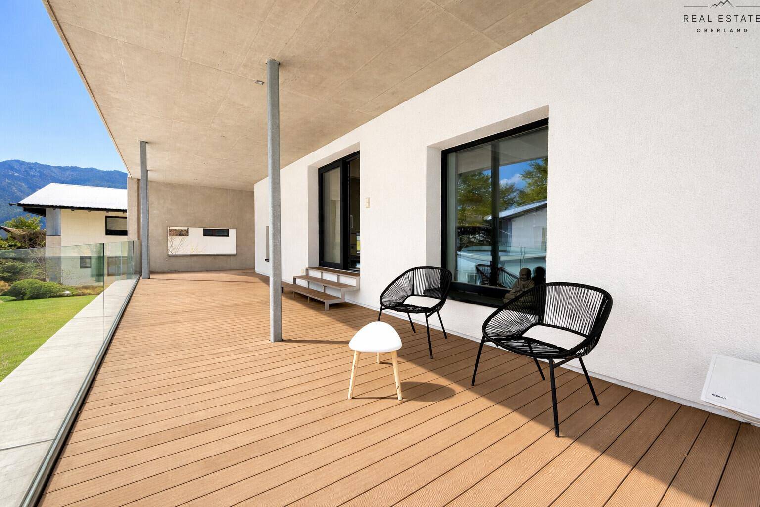 Große Holzterrasse mit modernen Gartenmöbeln und weitem Blick auf die Berge.