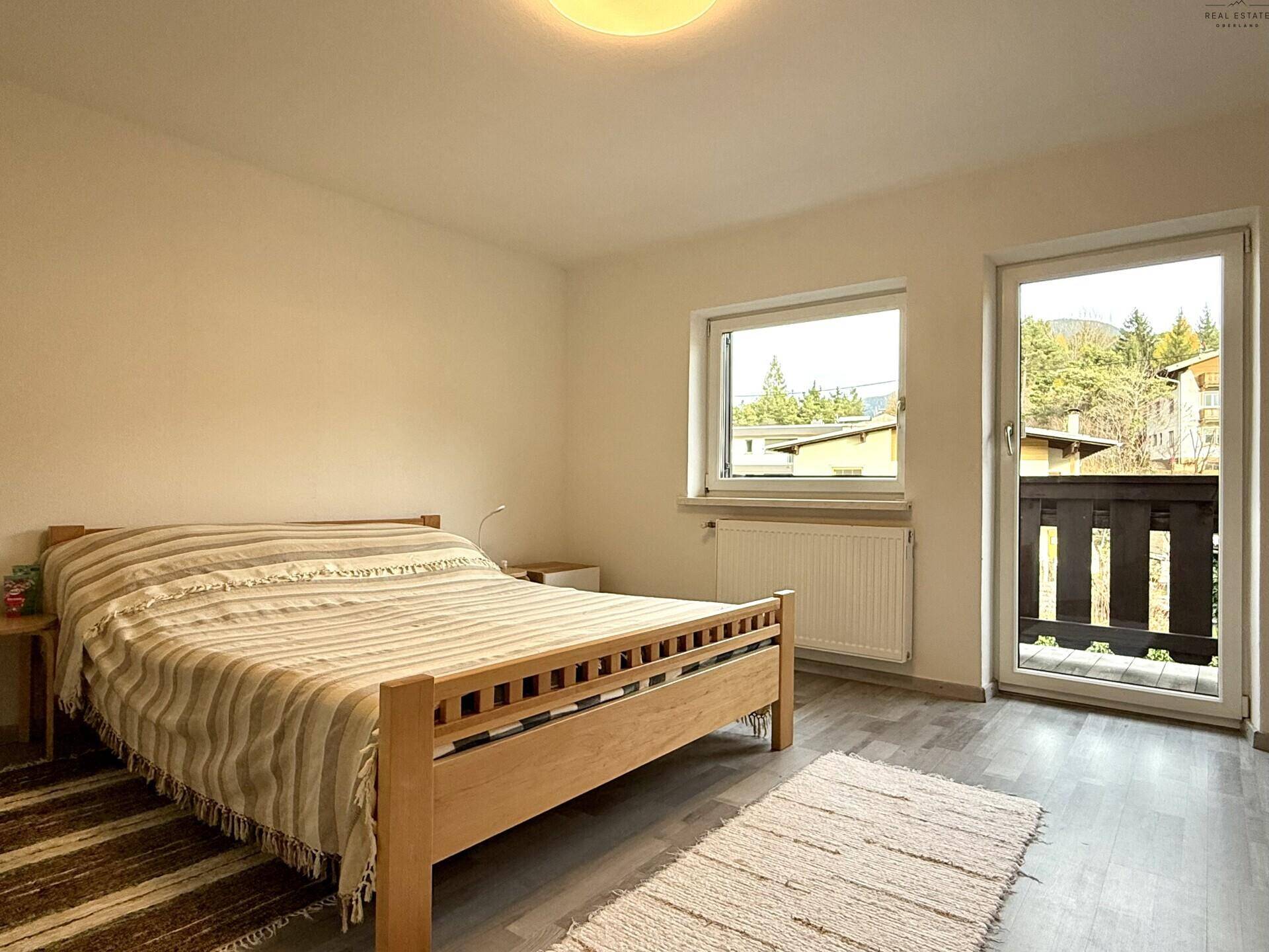 Schlafzimmer mit Holzbett, Laminatboden und Zugang zum Balkon.