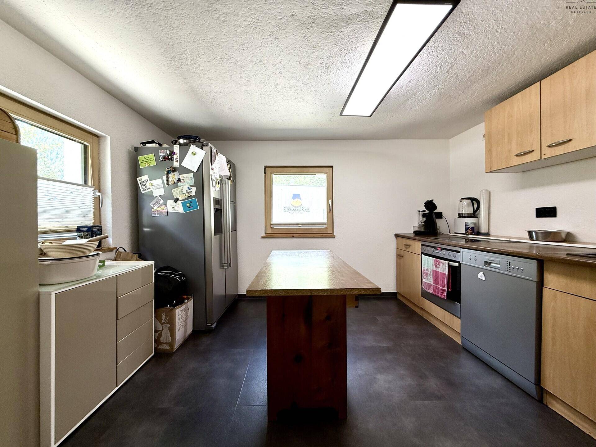 Geräumige Küche mit Holzschränken, dunklem Boden und einem großen Kühlschrank.