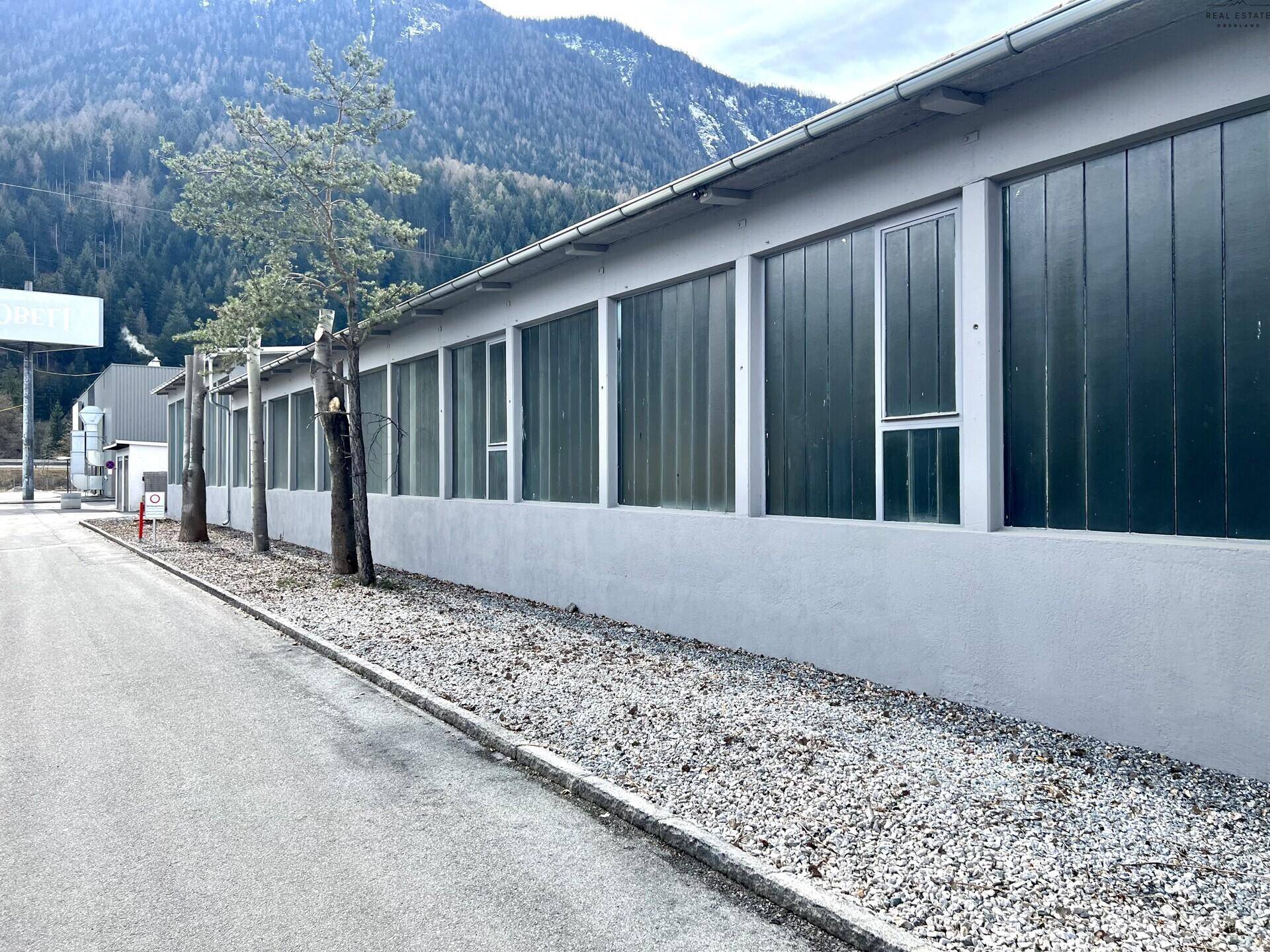 Seitenansicht des Industriegebäudes mit langen Fensterreihen und einem Schotterstreifen entlang der Fassade.