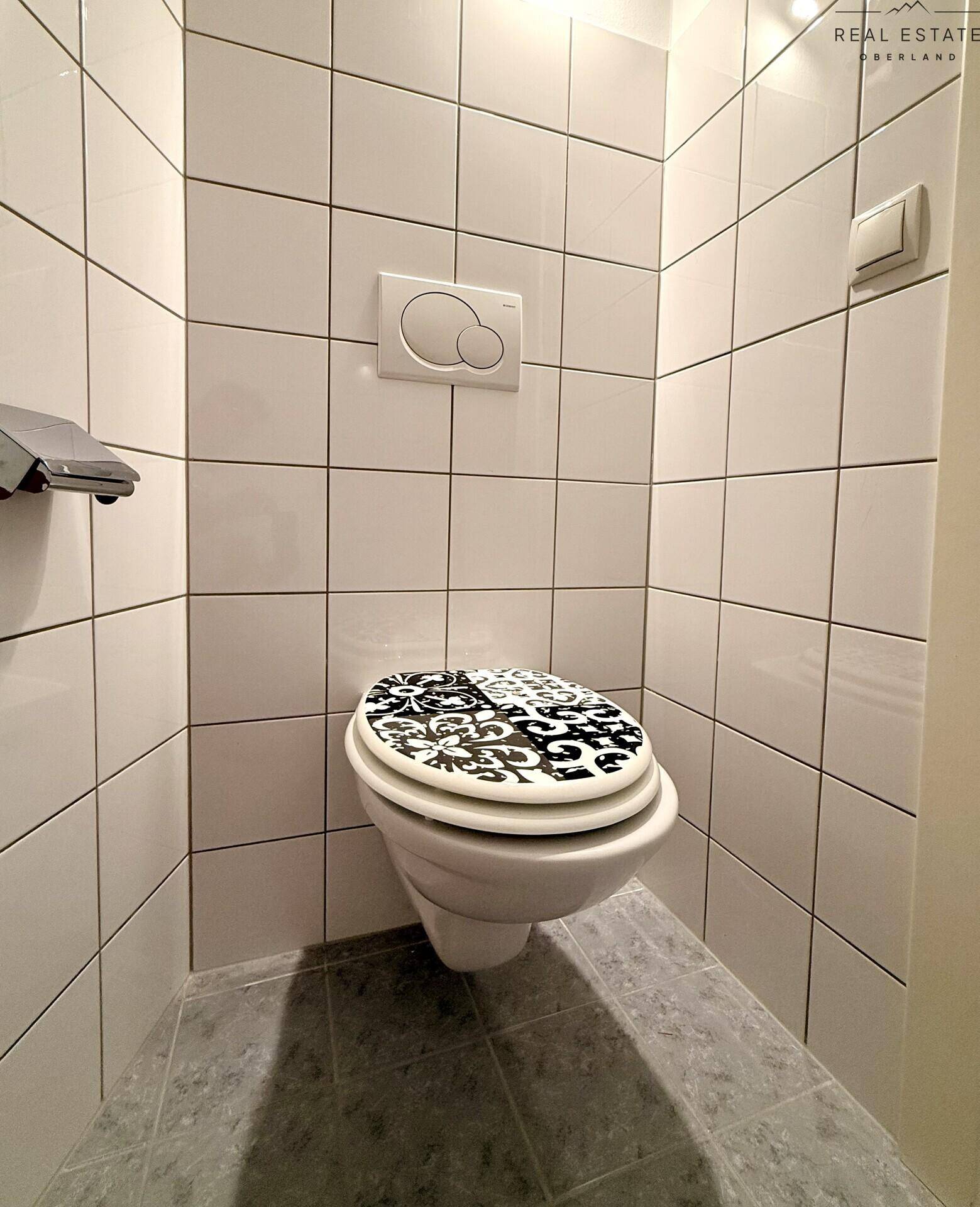 Separate Toilette mit Wand-WC und weißen Fliesen an den Wänden.