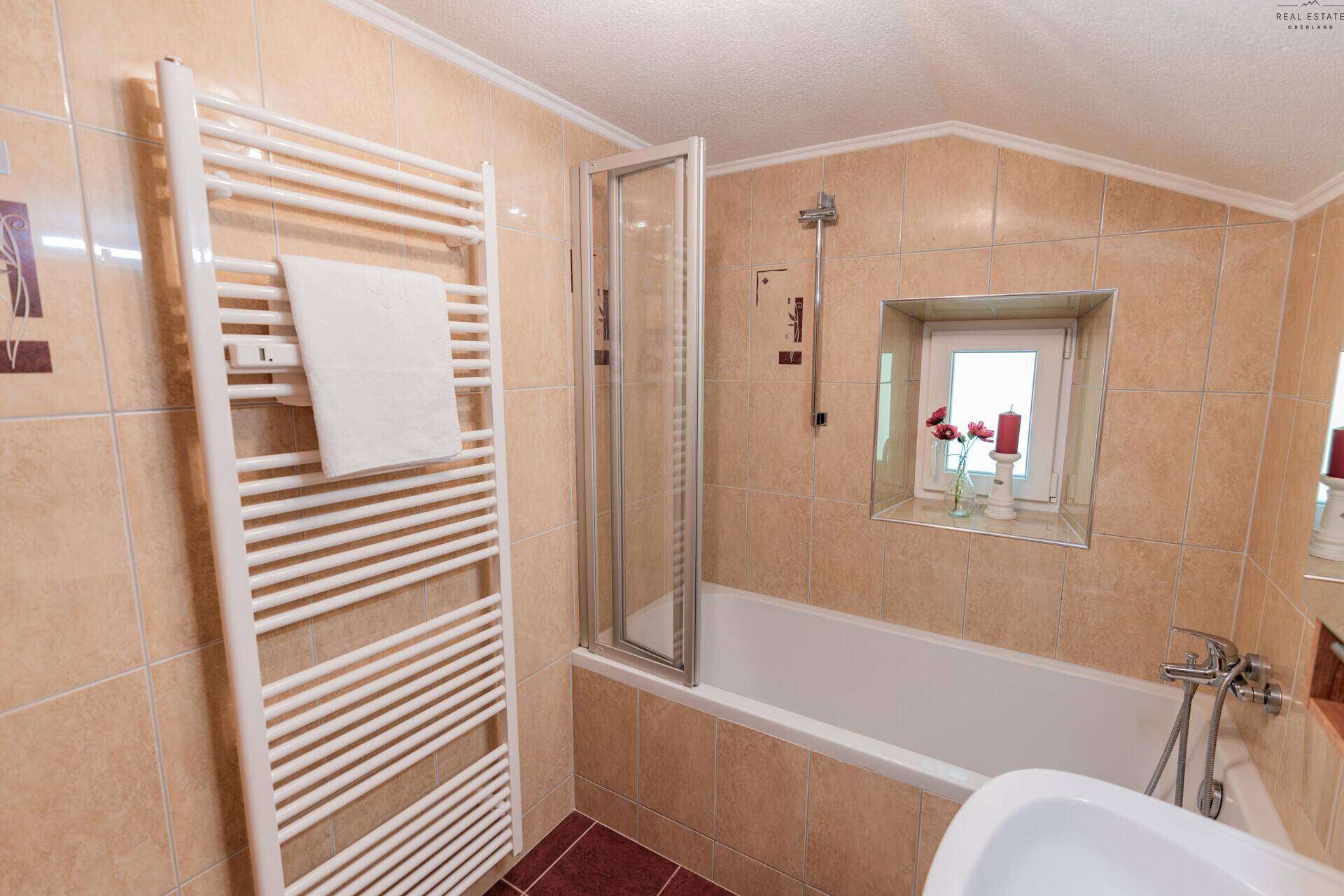Badezimmer mit beheiztem Handtuchhalter, Badewanne und Duschabtrennung.