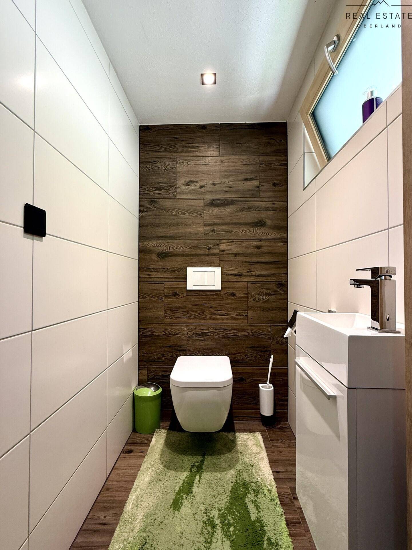 Modernes Gäste-WC mit Wand-WC, kleinem Waschbecken und Holzwandverkleidung.