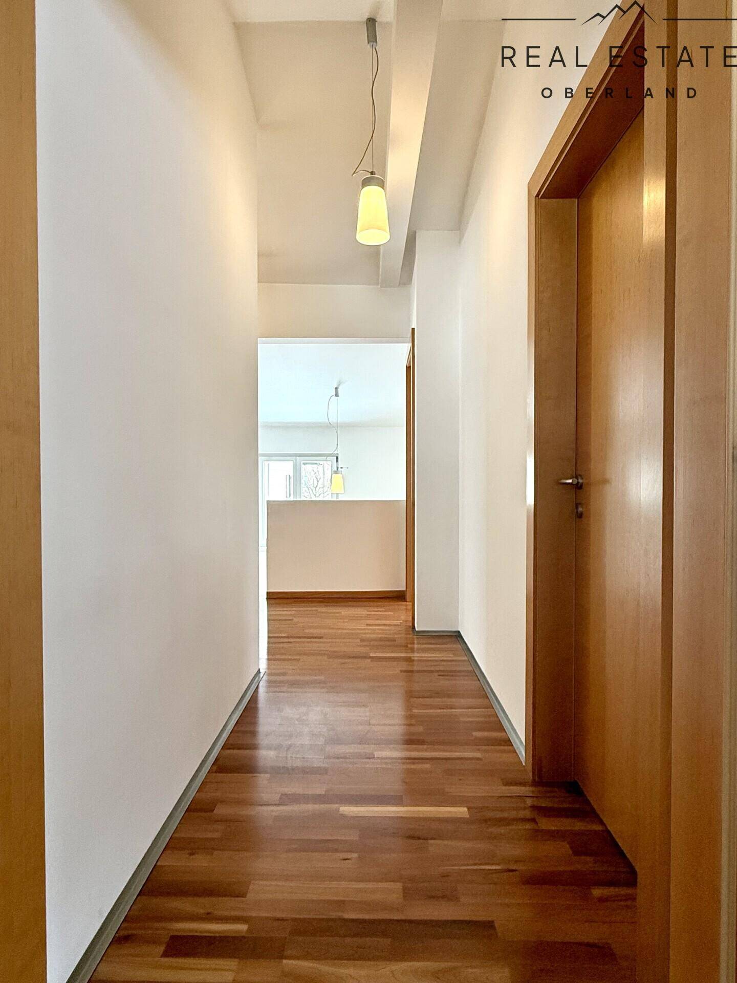 Langer, heller Flur mit durchgehendem Holzfußboden, der zu verschiedenen Zimmern der Wohnung führt.