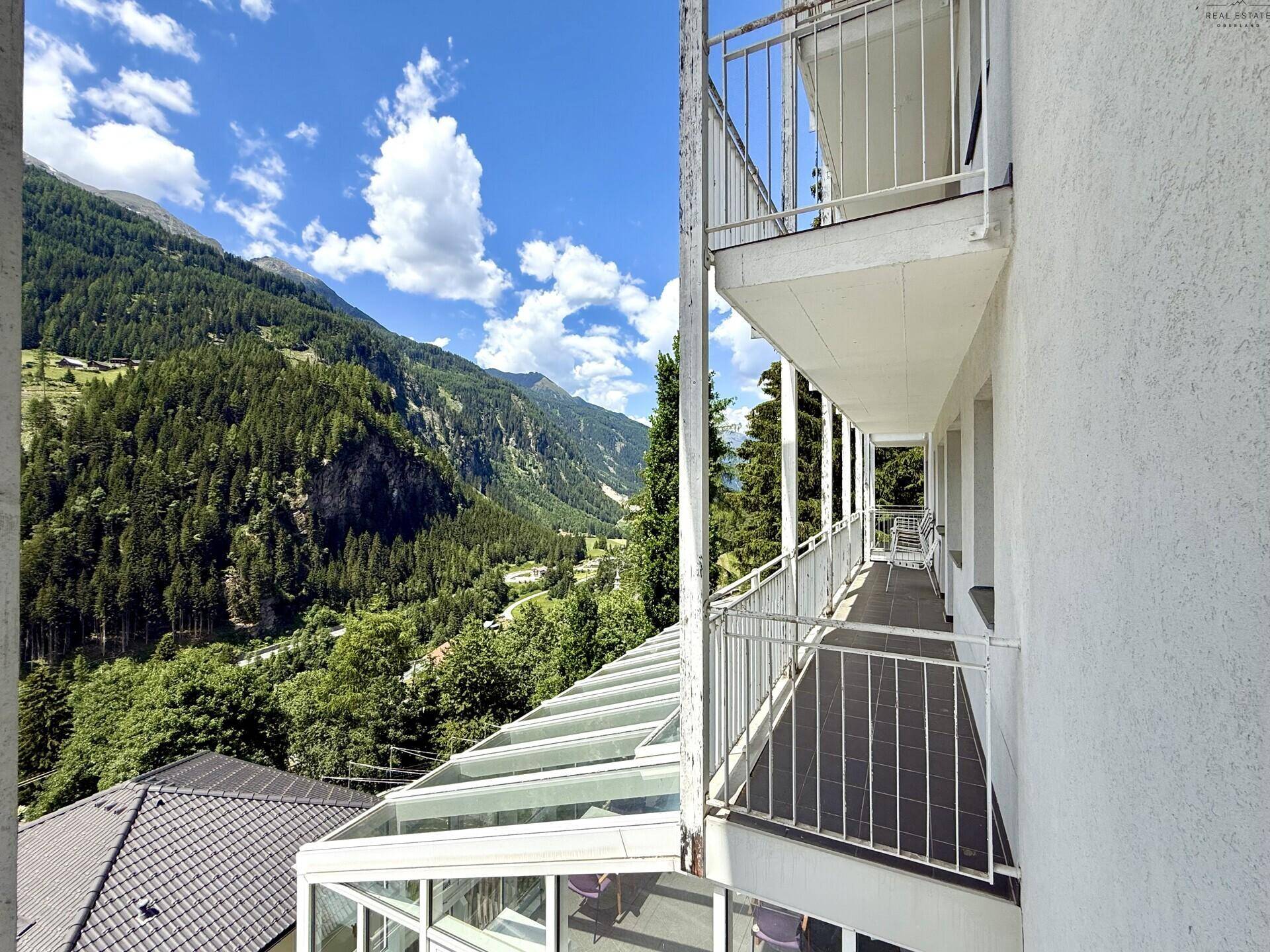 Langer Balkon mit atemberaubendem Bergblick und Glasdach über dem unteren Bereich.