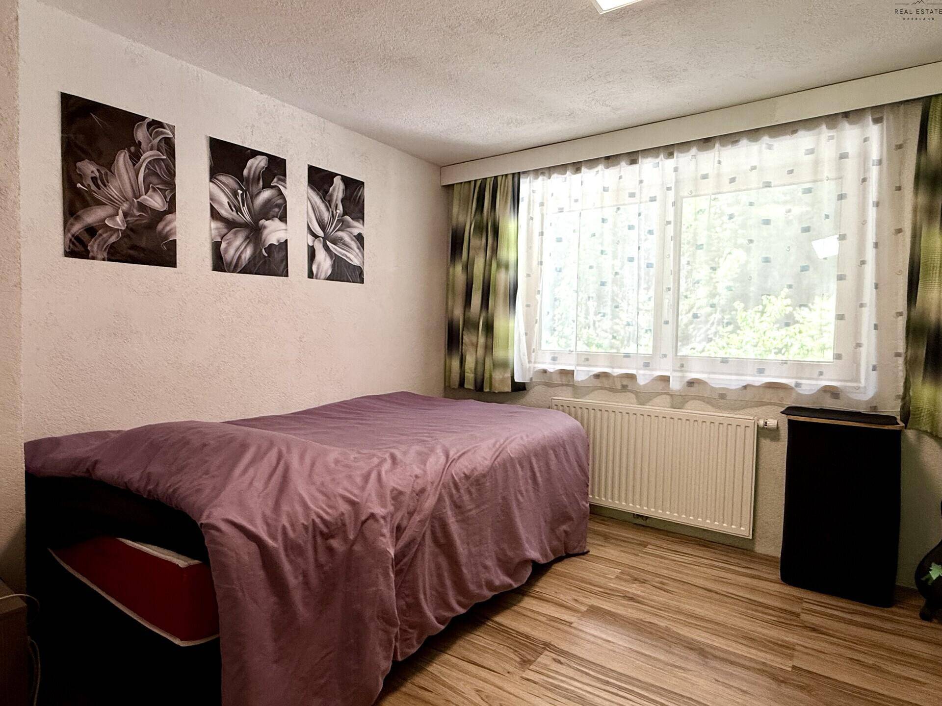 Gemütliches Schlafzimmer mit Einzelbett, Holzfußboden und Blick ins Grüne.