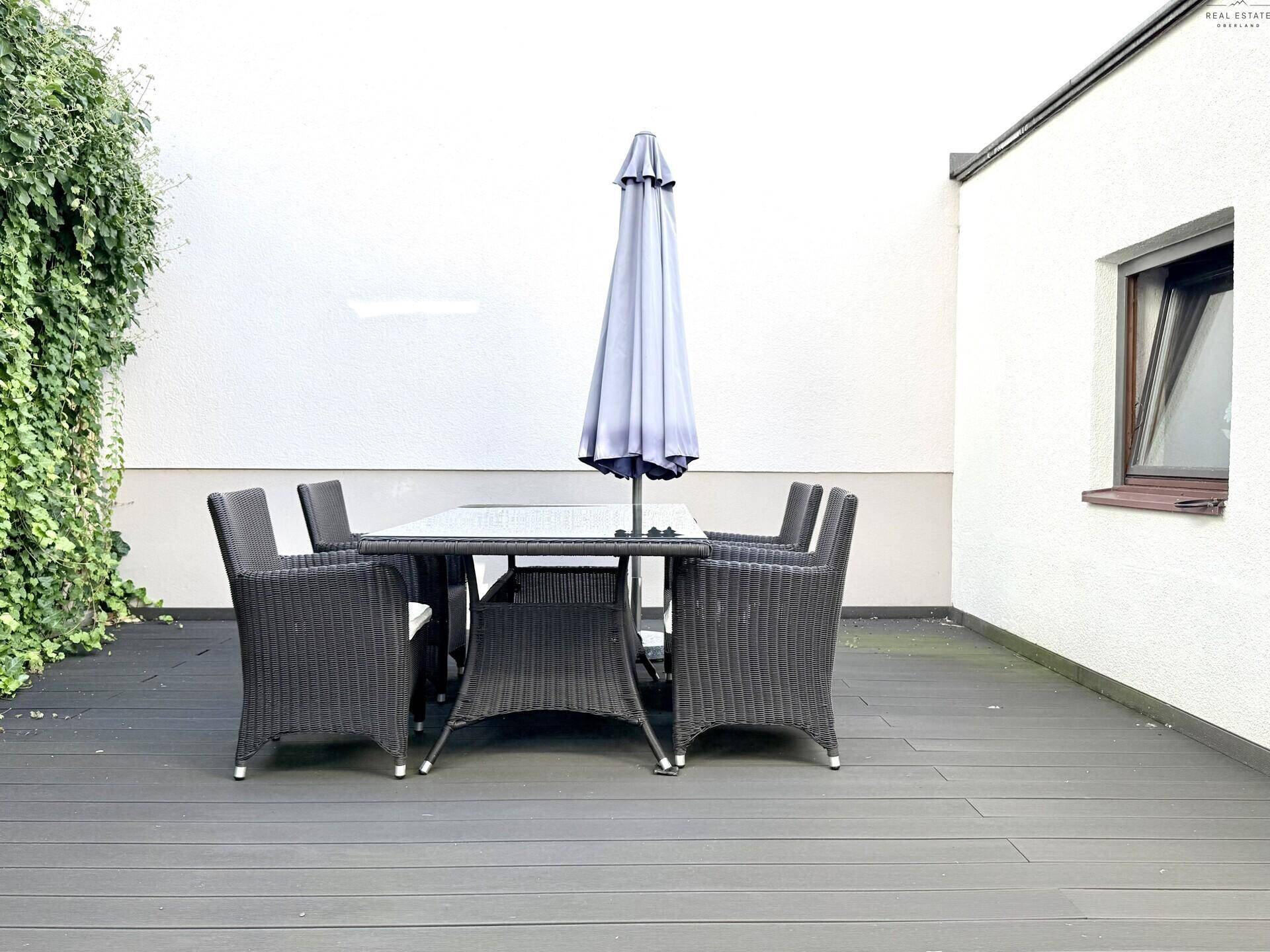 Geräumige Terrasse mit Esstisch, Sonnenschirm und dunklem Holzboden.