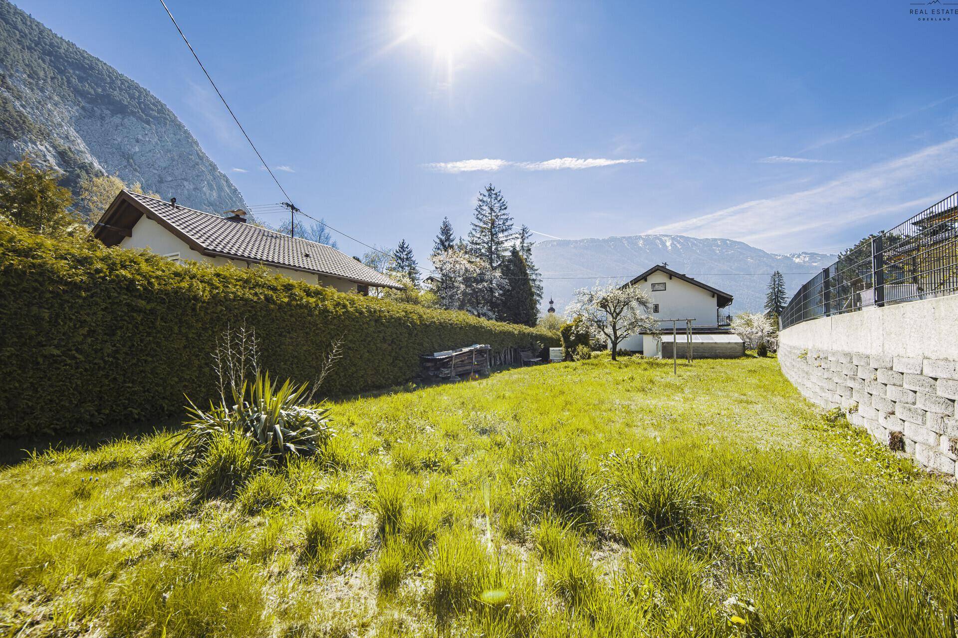 Sonnige Rasenfläche im Garten mit Hecke und beeindruckendem Bergblick.