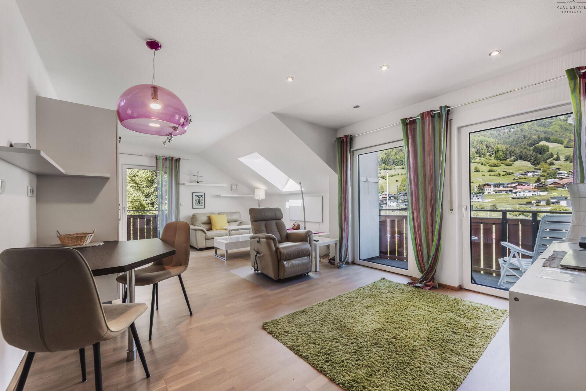 Helles Wohnzimmer in einer Dachgeschosswohnung mit Balkonzugang und Bergblick.