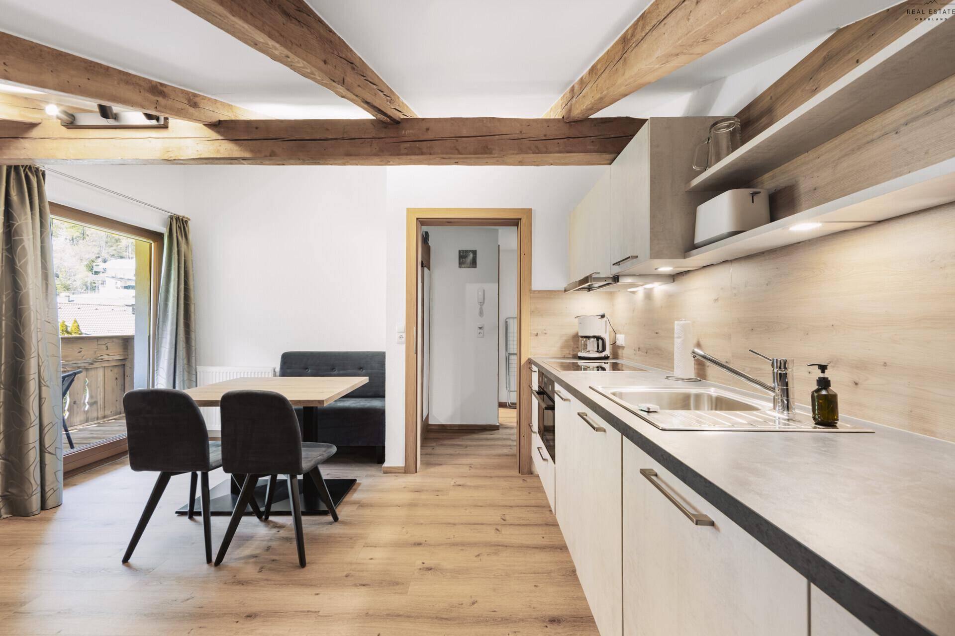 Moderne Wohnküche mit Essbereich, Holzbalken und Zugang zu einem Balkon.