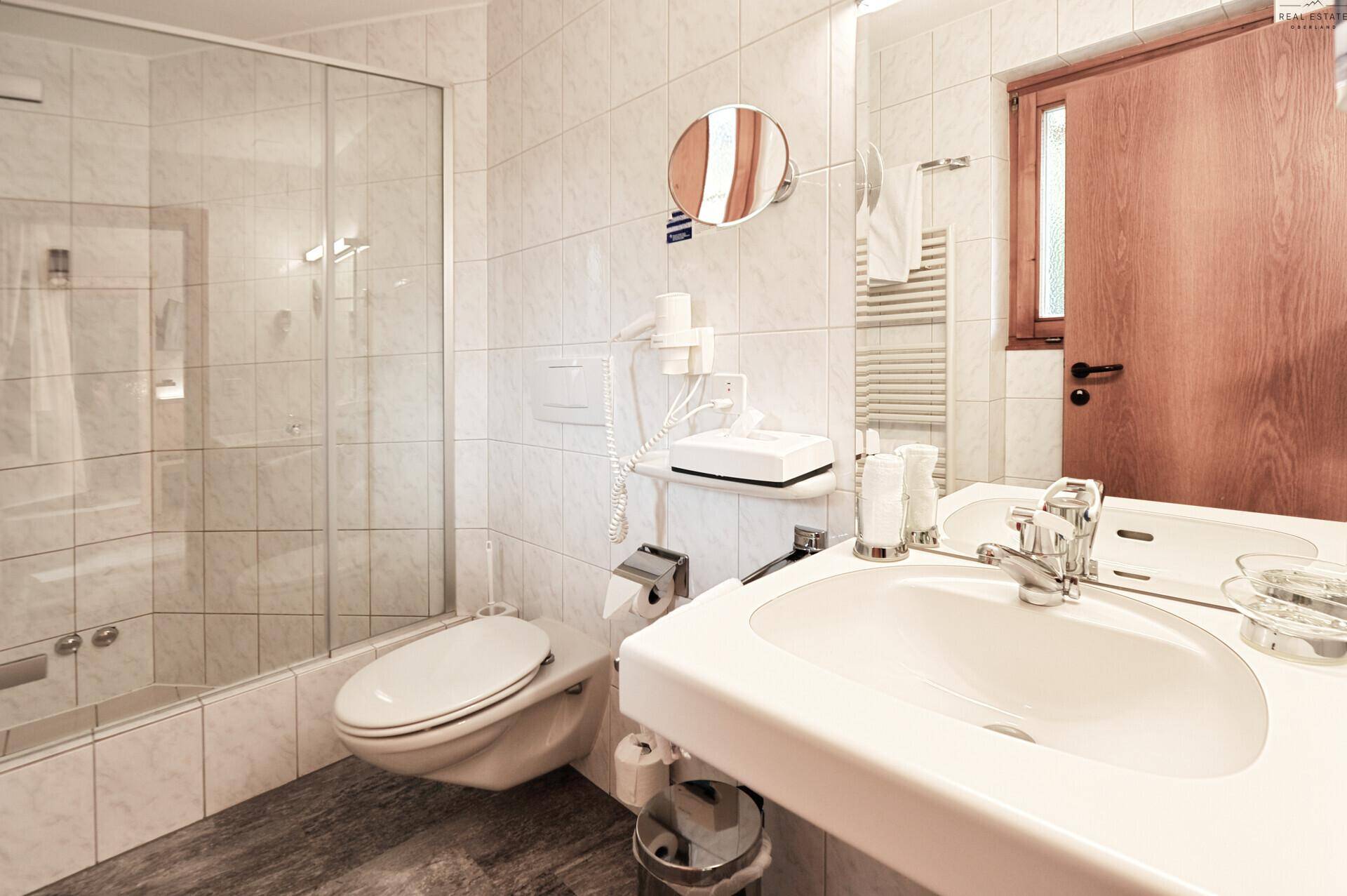 Badezimmer mit Duschkabine, WC, Waschbecken und hellen Wandfliesen.