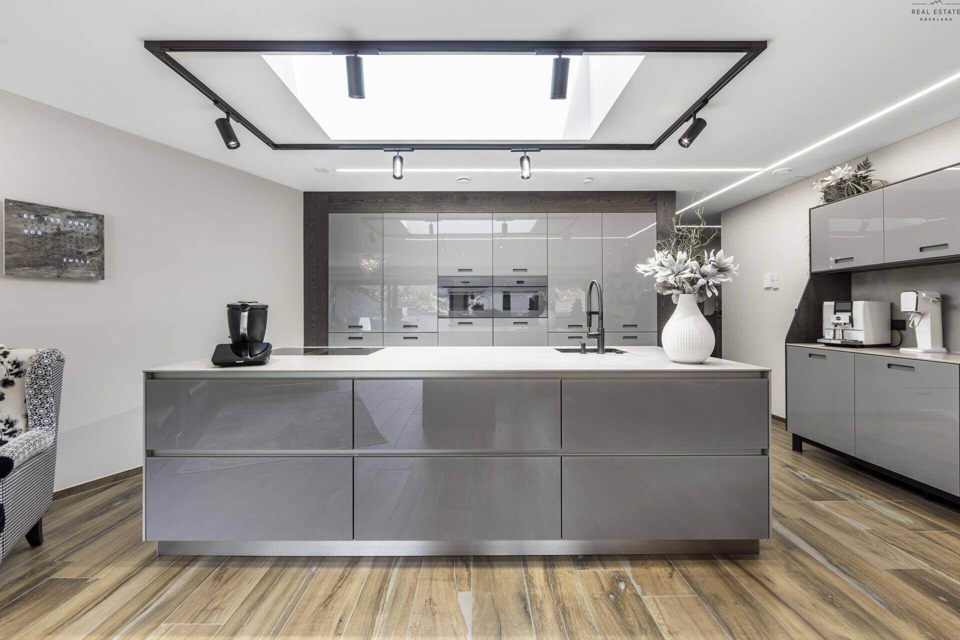 Elegante, moderne Küche mit großer Kochinsel, integrierten Geräten und glänzenden grauen Fronten.