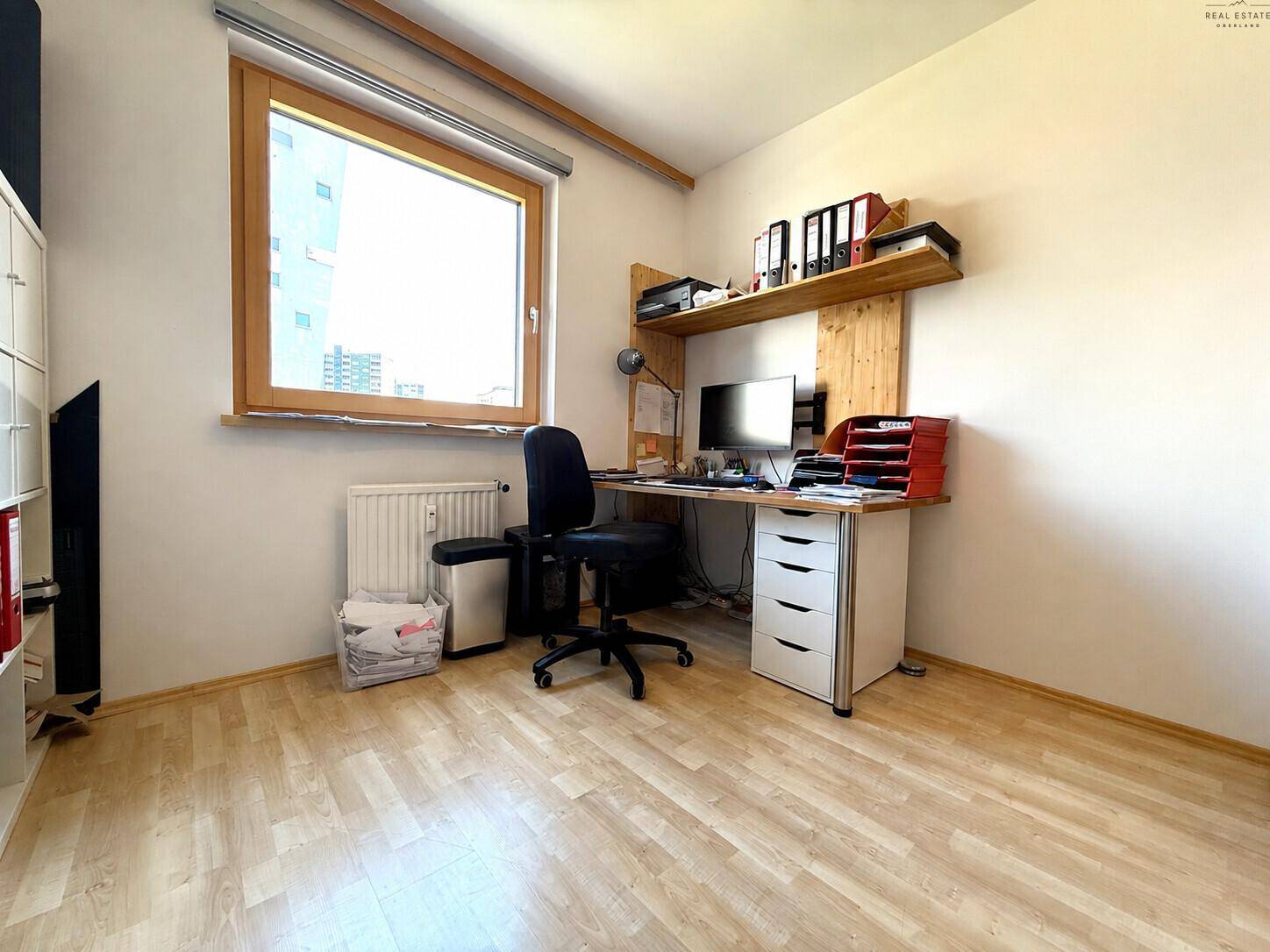 Arbeitsbereich mit Holzschreibtisch, Wandregal und Blick aus dem Fenster.