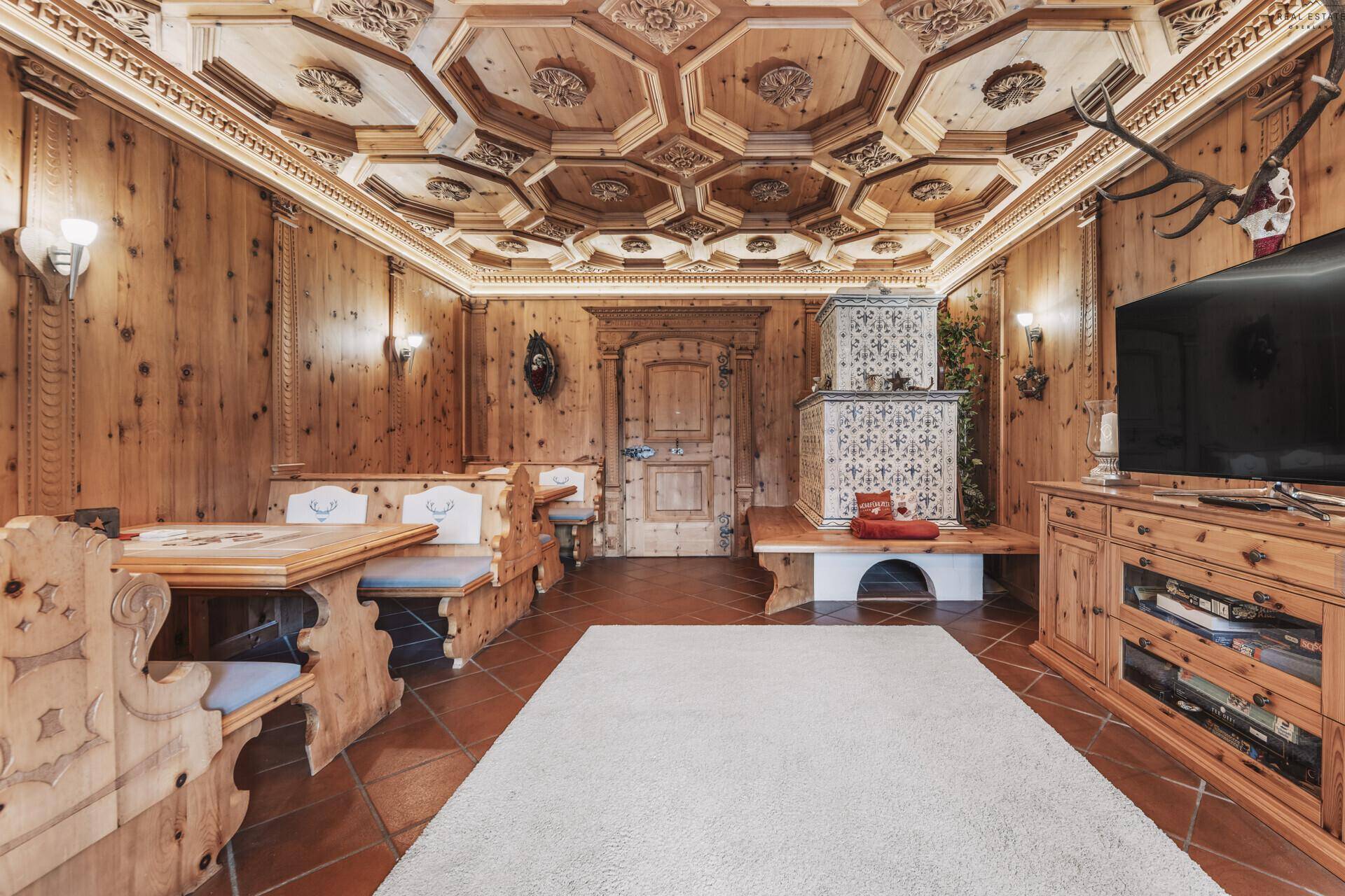 Traditionelles alpines Wohnzimmer mit aufwendiger Holzvertäfelung, Kachelofen und geschnitzter Decke.