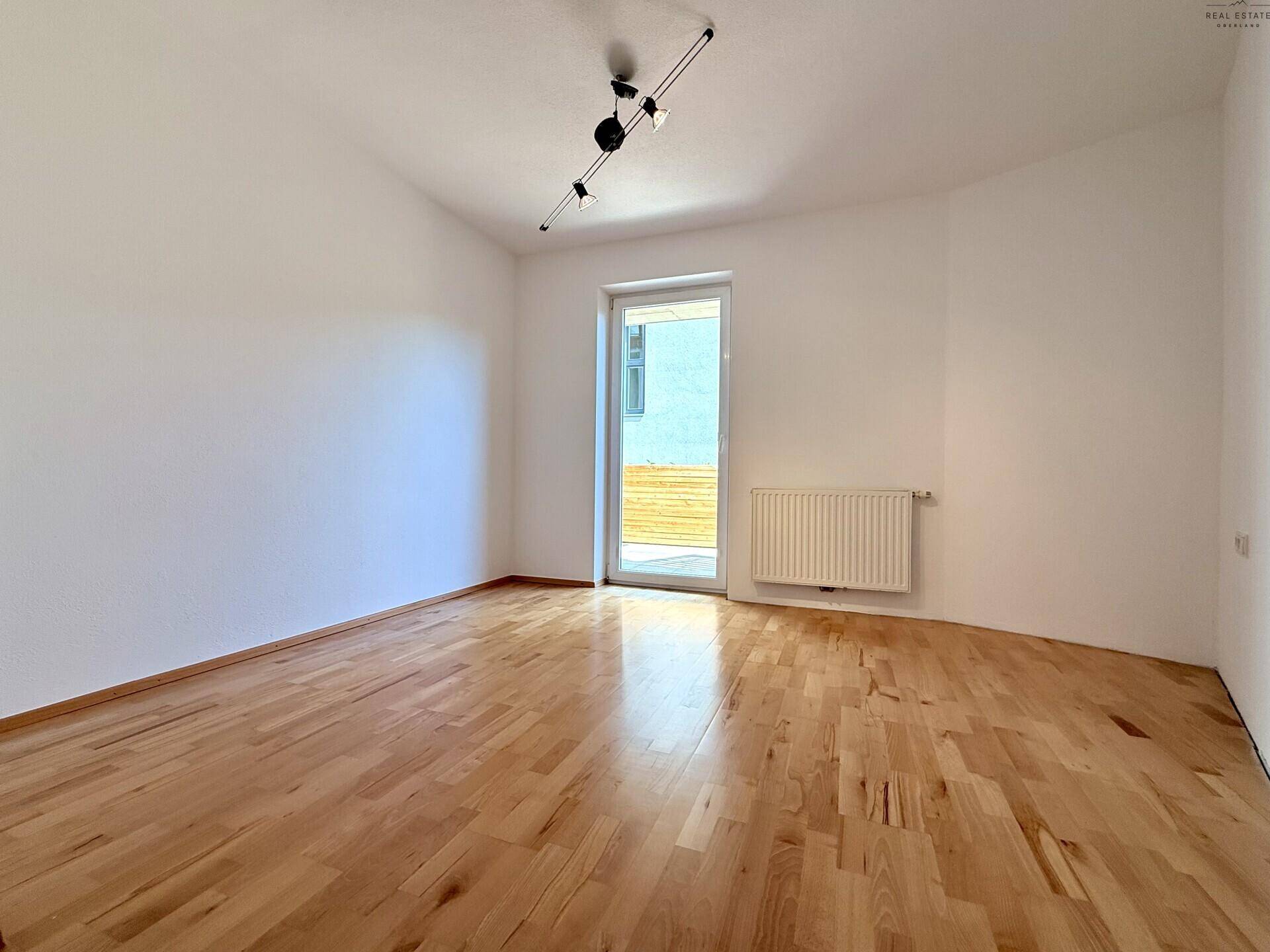 Helles Schlafzimmer mit Holzboden, Heizkörper und Zugang zu einem Außenbereich.