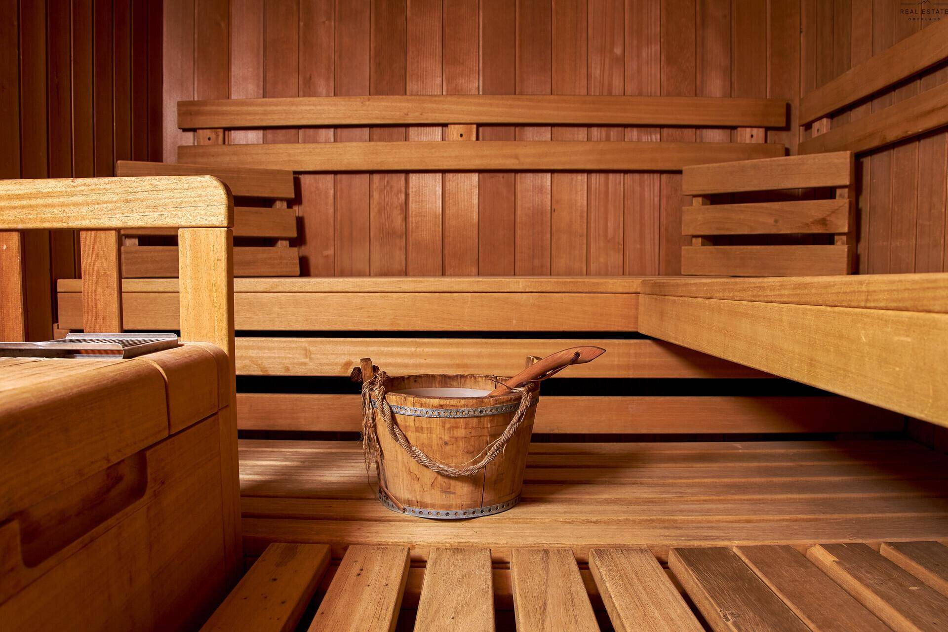 Traditionelle Holzsauna mit mehreren Bänken und einem Holzeimer für Aufgüsse.