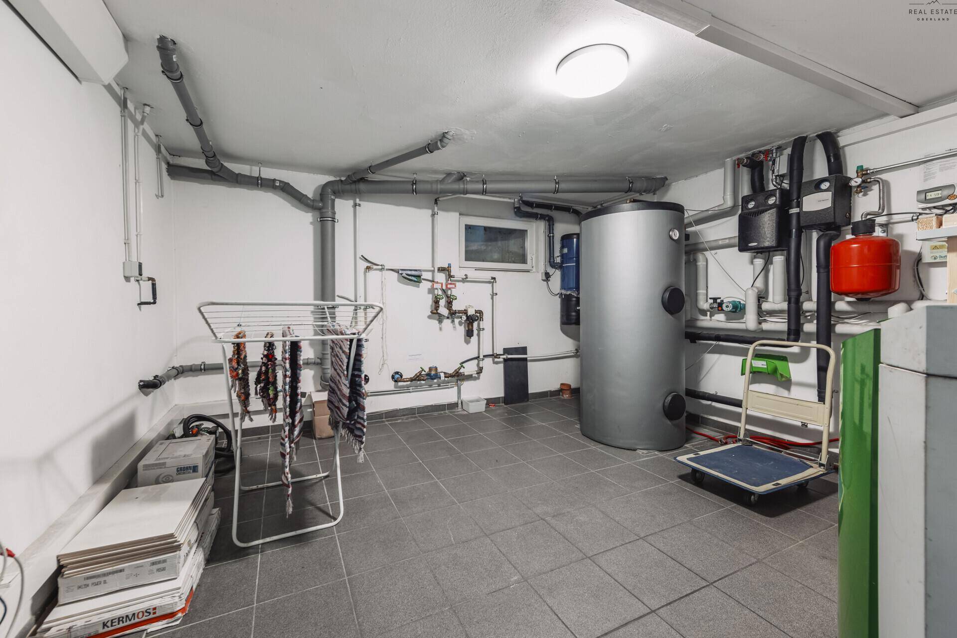 Heizungsraum im Keller mit Warmwasserspeicher, Leitungen und Wäscheständer.