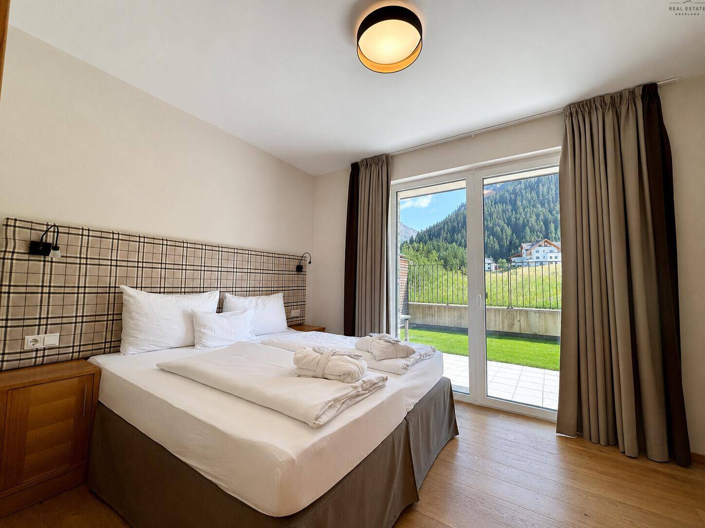 Gemütliches Schlafzimmer mit Doppelbett, Holzfußboden und Bergblick durch die Terrassentür.