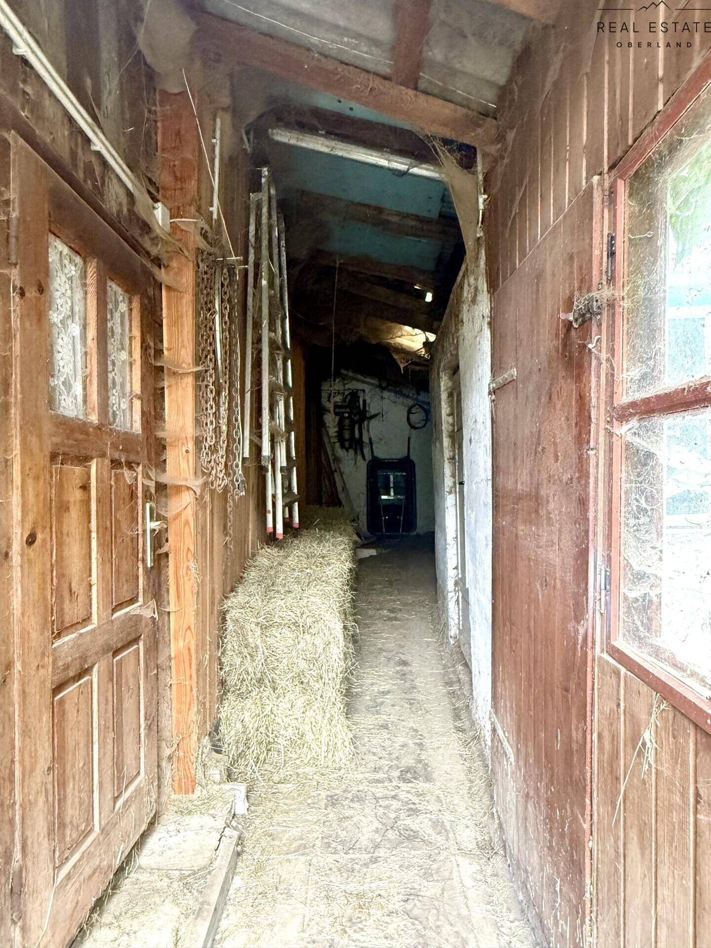 Innenansicht eines rustikalen Stalls mit Holztüren und Heuballen, renovierungsbedürftig.