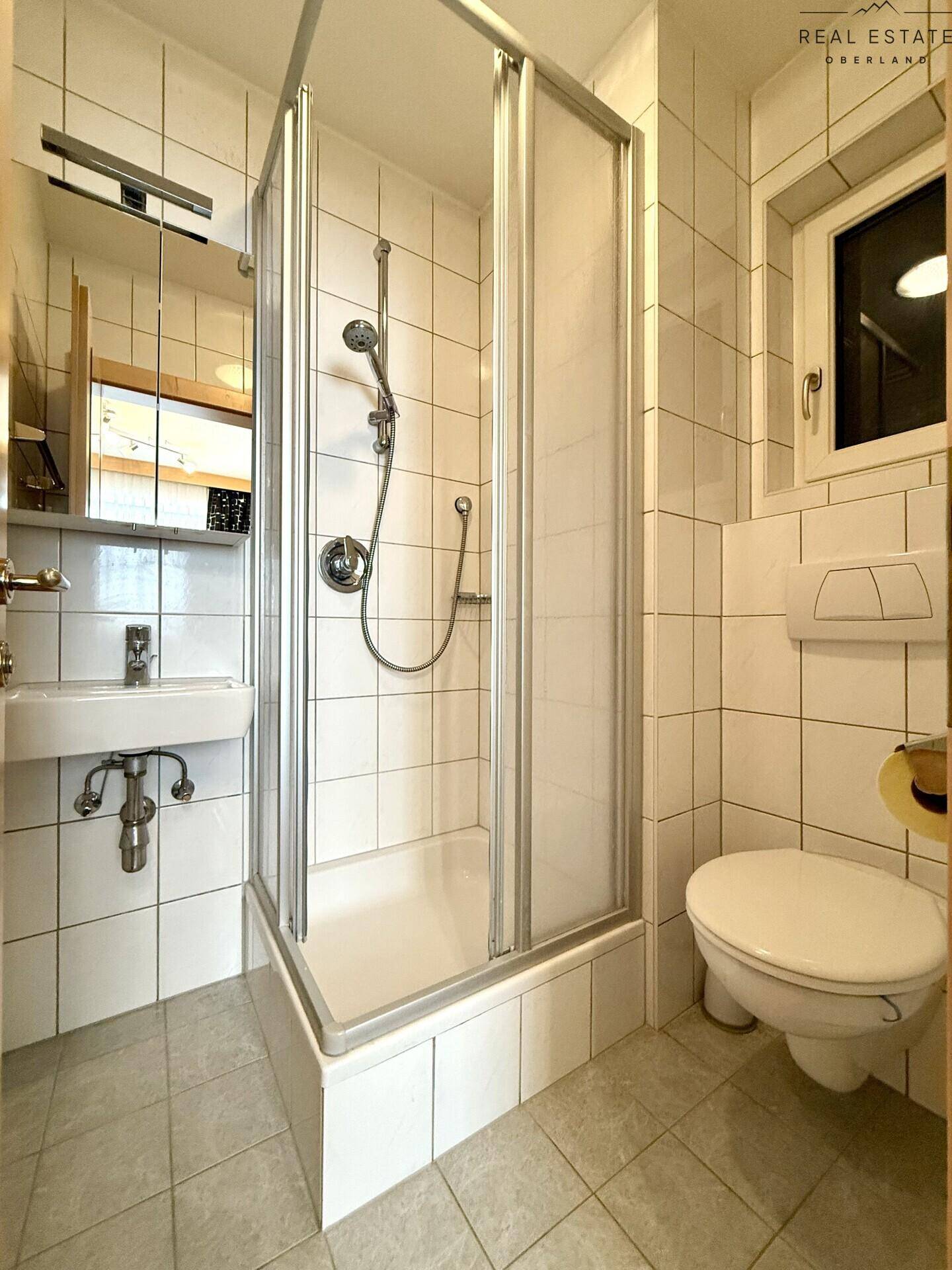 Kleines Badezimmer mit Dusche, WC, Waschbecken und Fenster.