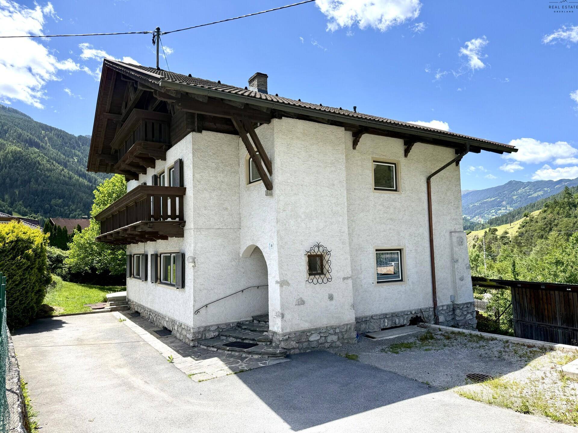 Ansicht des Hauses mit traditionellen Holzbalkonen und gepflasterter Zufahrt.