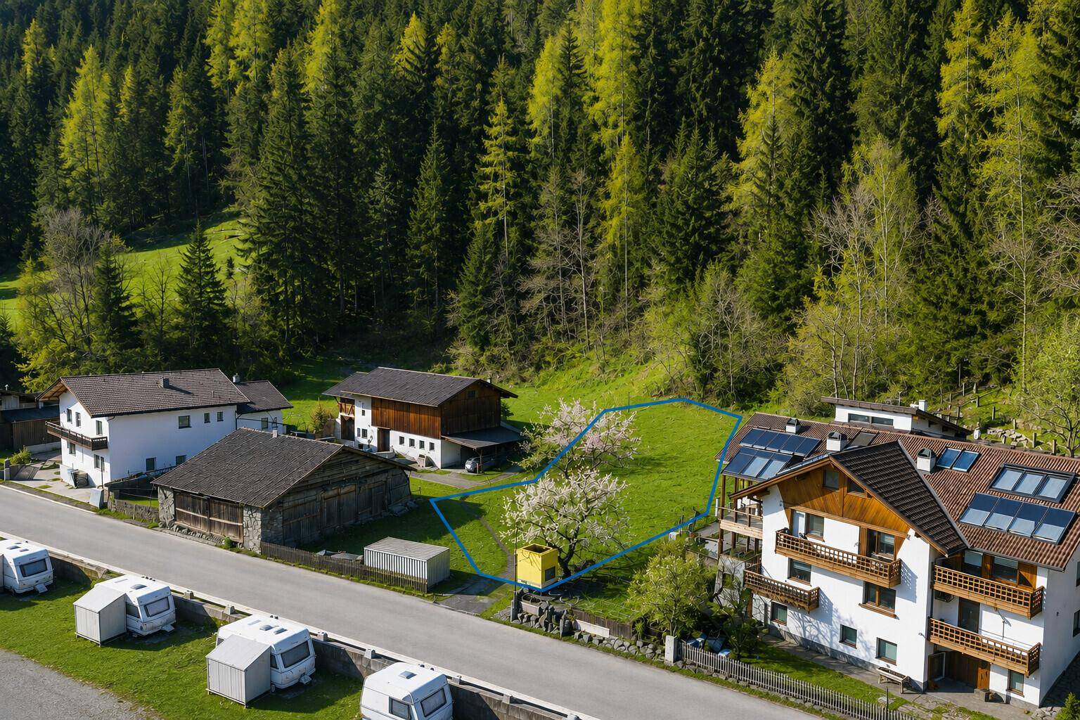 Übersicht aus der Vogelperspektive eines grünen Grundstücks mit angrenzenden Gebäuden und Wald.