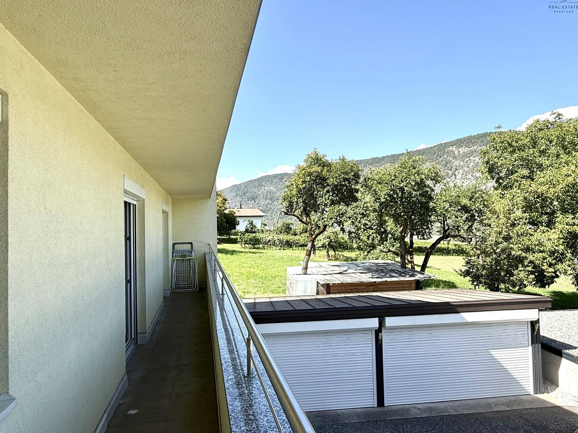 Langer Balkon mit Metallgeländer und Blick auf den Garten sowie die umliegende Landschaft.