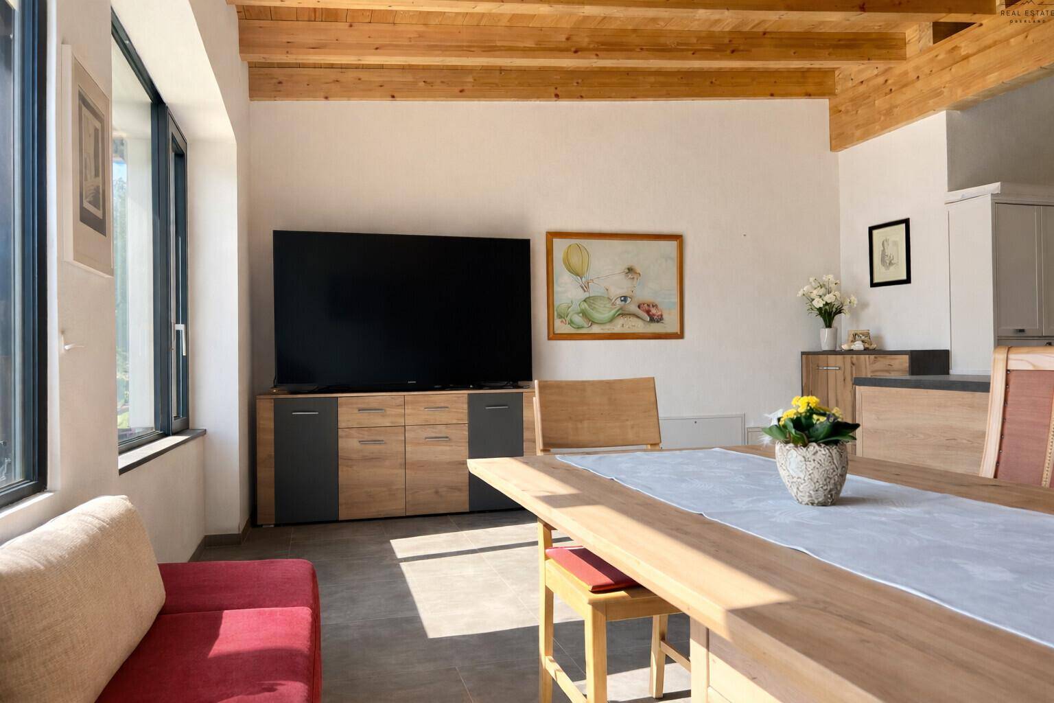 Lichtdurchfluteter Wohn- und Essbereich mit großen Fenstern, Holzbalkendecke und modernem Sideboard.