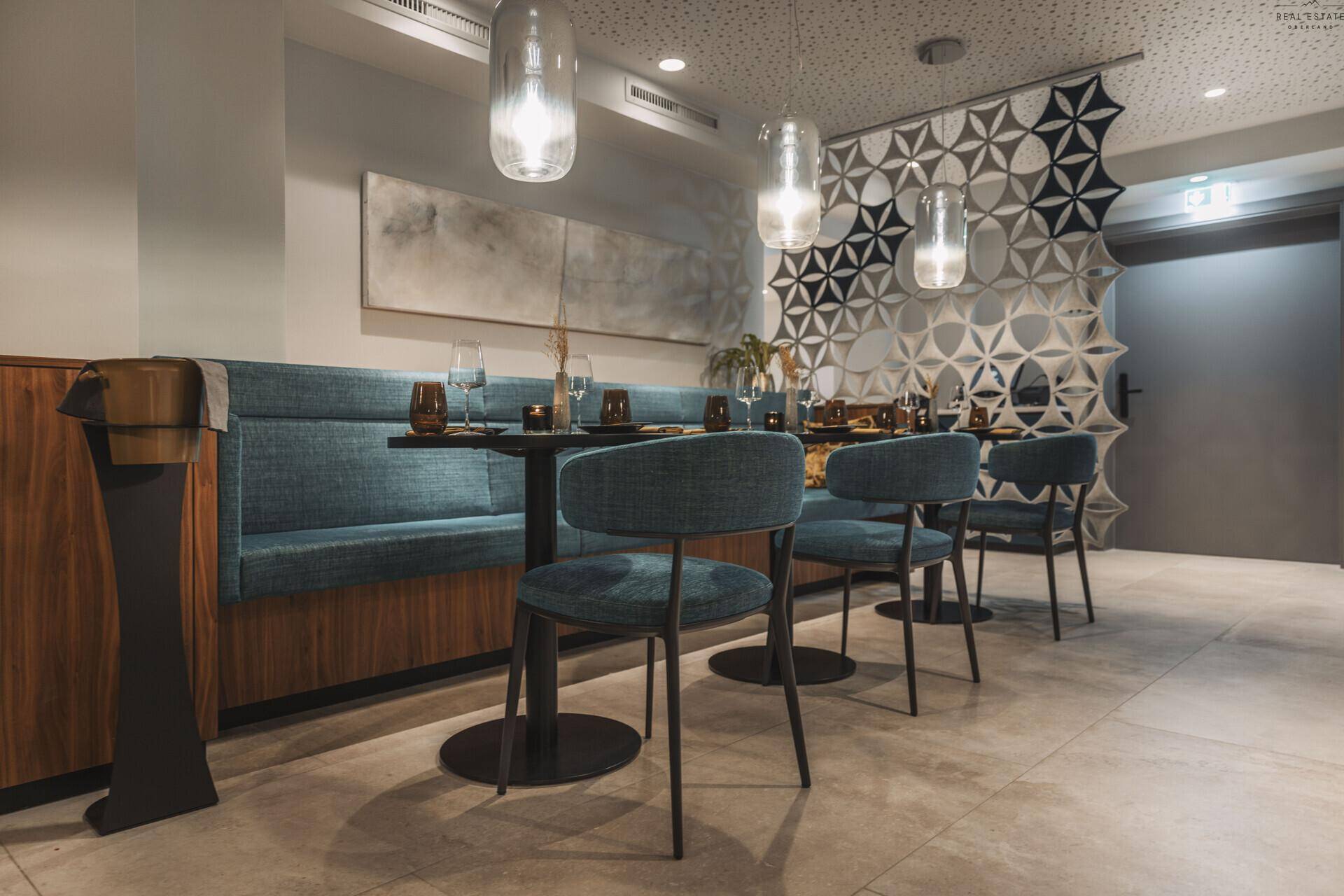 Stilvoller Restaurantbereich mit blauer Sitzbank, dunklen Tischen und moderner Beleuchtung.
