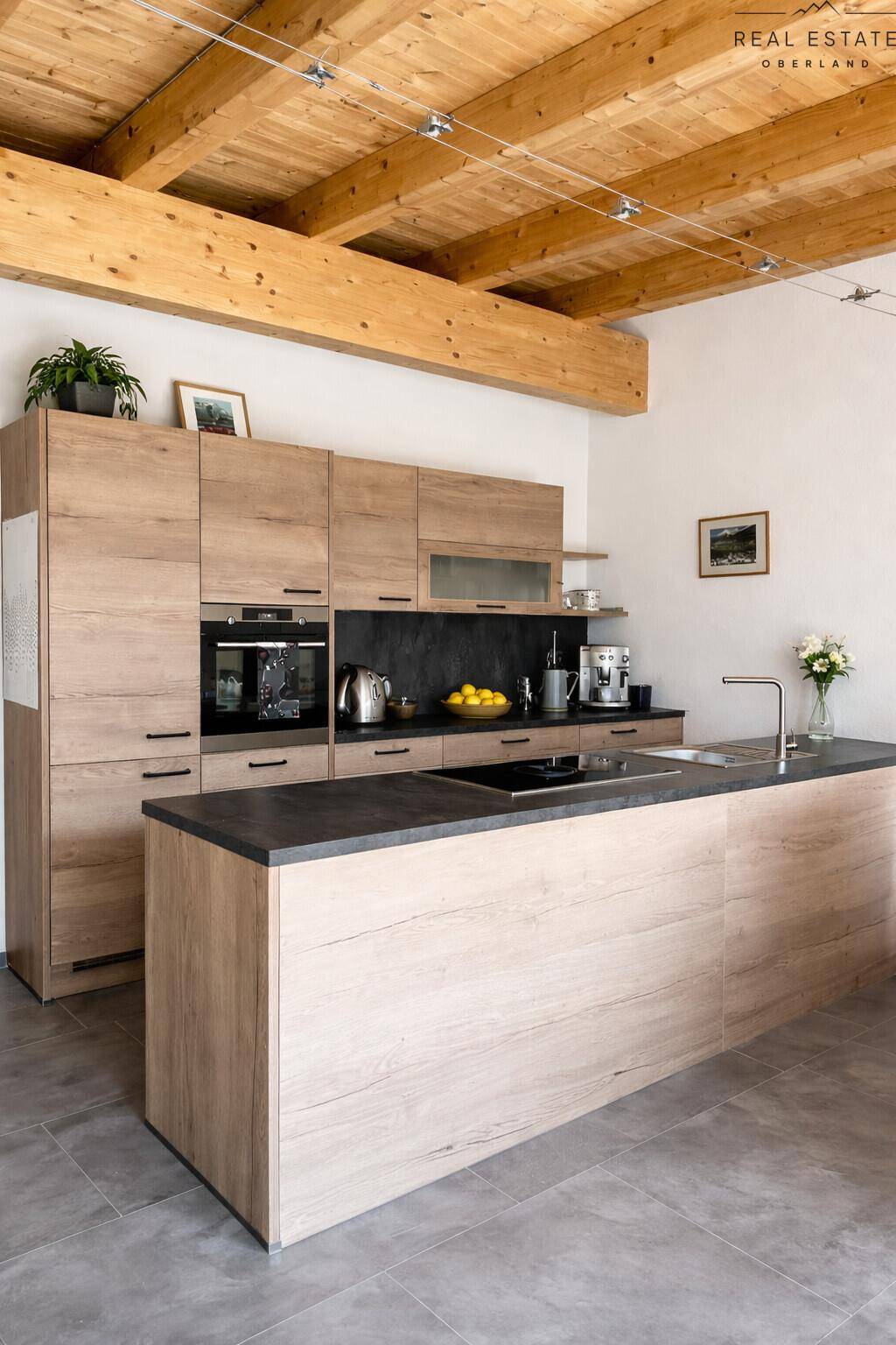 Helle, moderne Küche mit Holzfronten, Kücheninsel und dunkler Arbeitsplatte unter Holzbalkendecke.