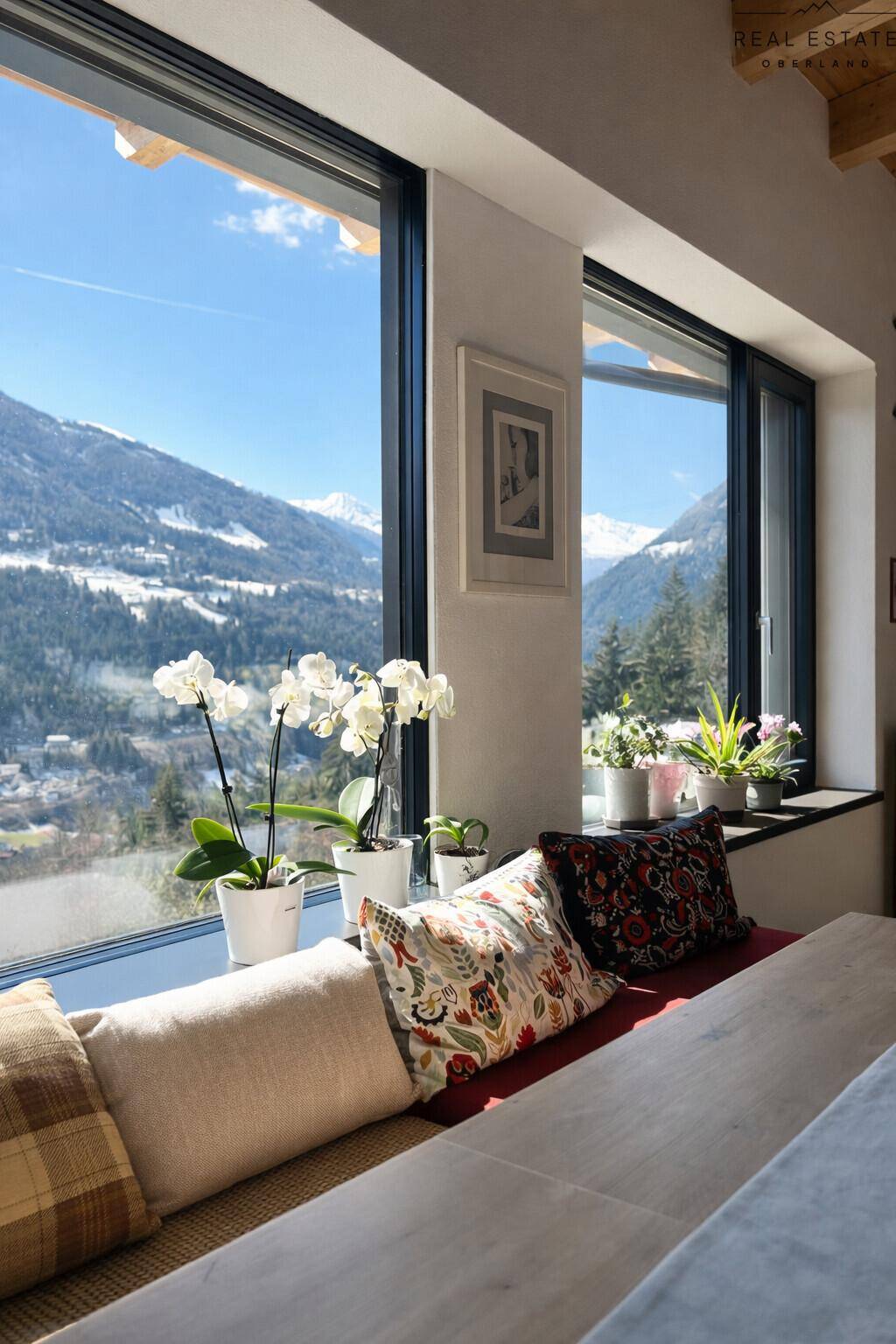 Heller Wohnbereich mit breiter Fensterbank, Kissen und weitem Blick auf die verschneiten Berge.