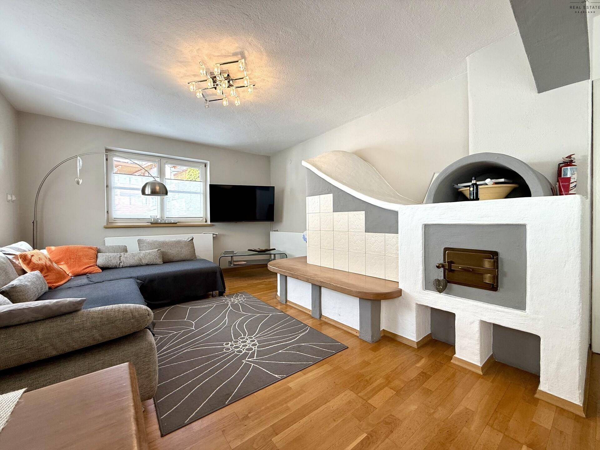 Wohnzimmer mit Kachelofen, Holzboden und bequemer Sofalandschaft.