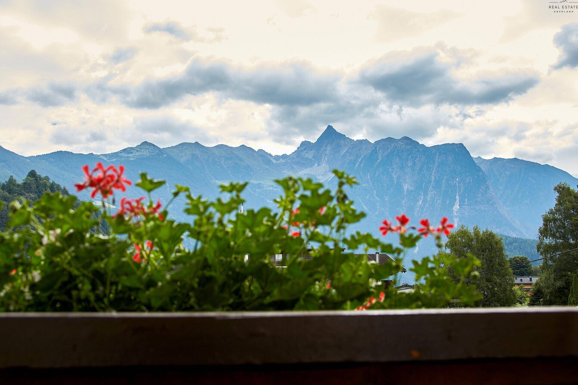 Balkon mit roten Blumenkästen und einem weiten Blick auf die majestätischen Berge.