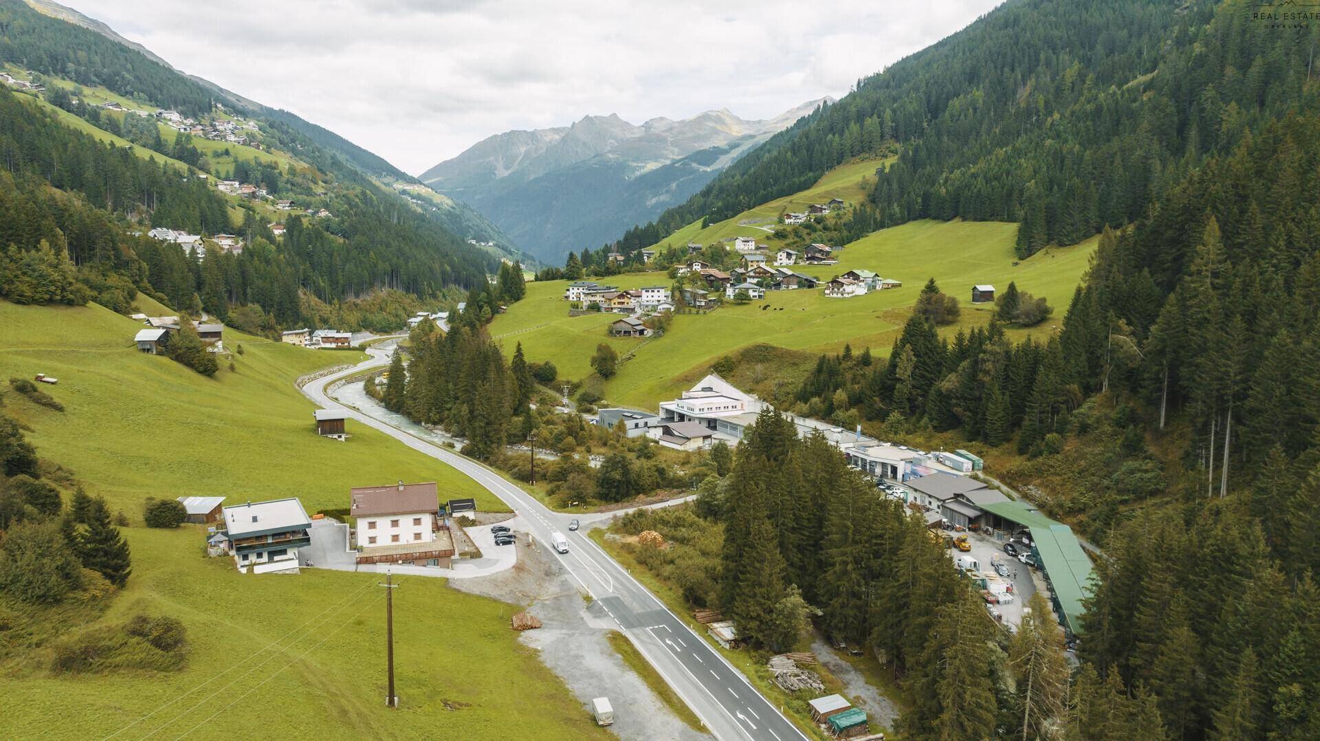 Weitläufige Luftaufnahme eines malerischen Tals mit einem Dorf, einer Straße und üppigen Wäldern.