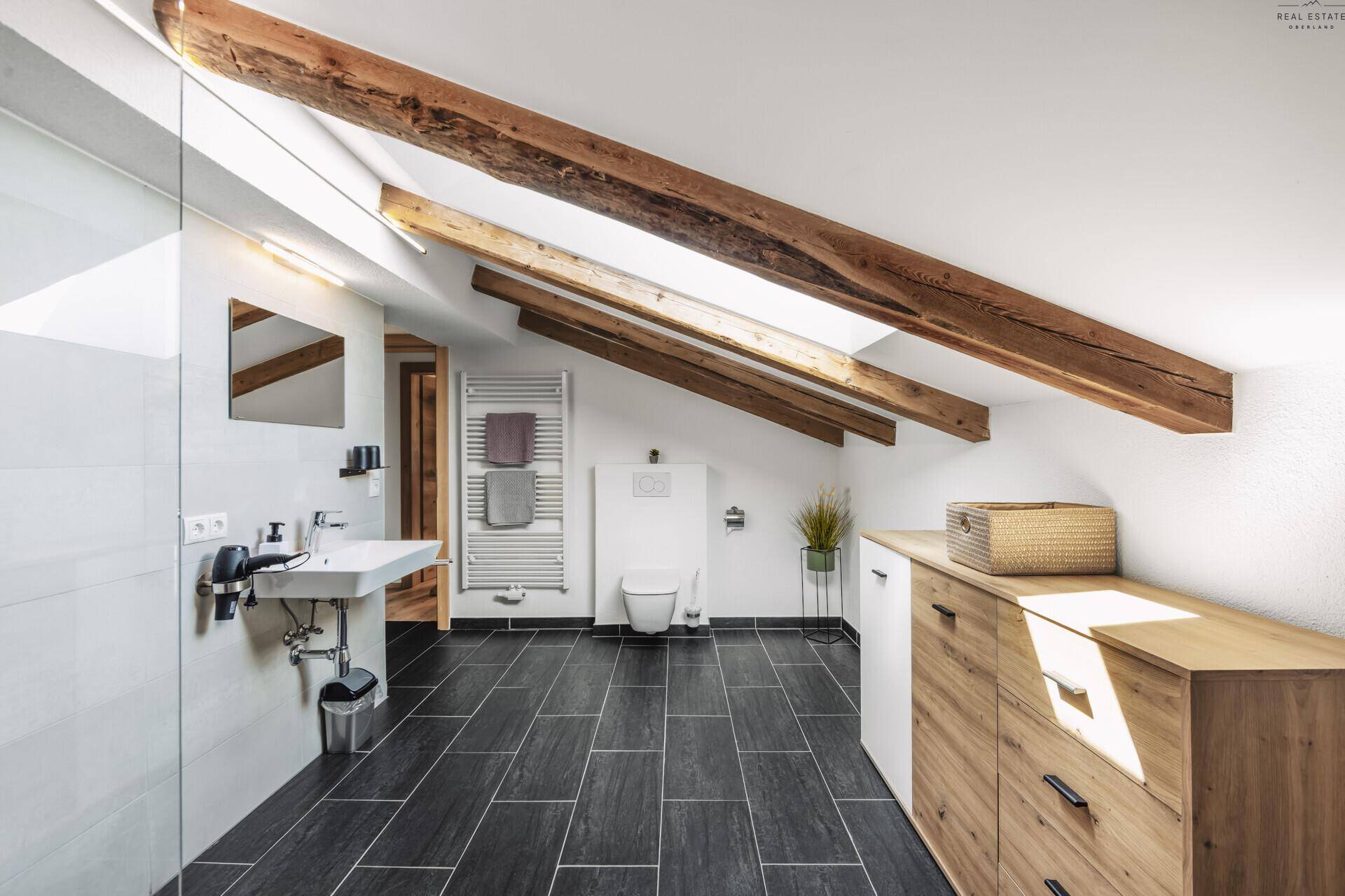 Geräumiges Badezimmer im Dachgeschoss mit begehbarer Dusche, Holzbalken und Dachfenster.