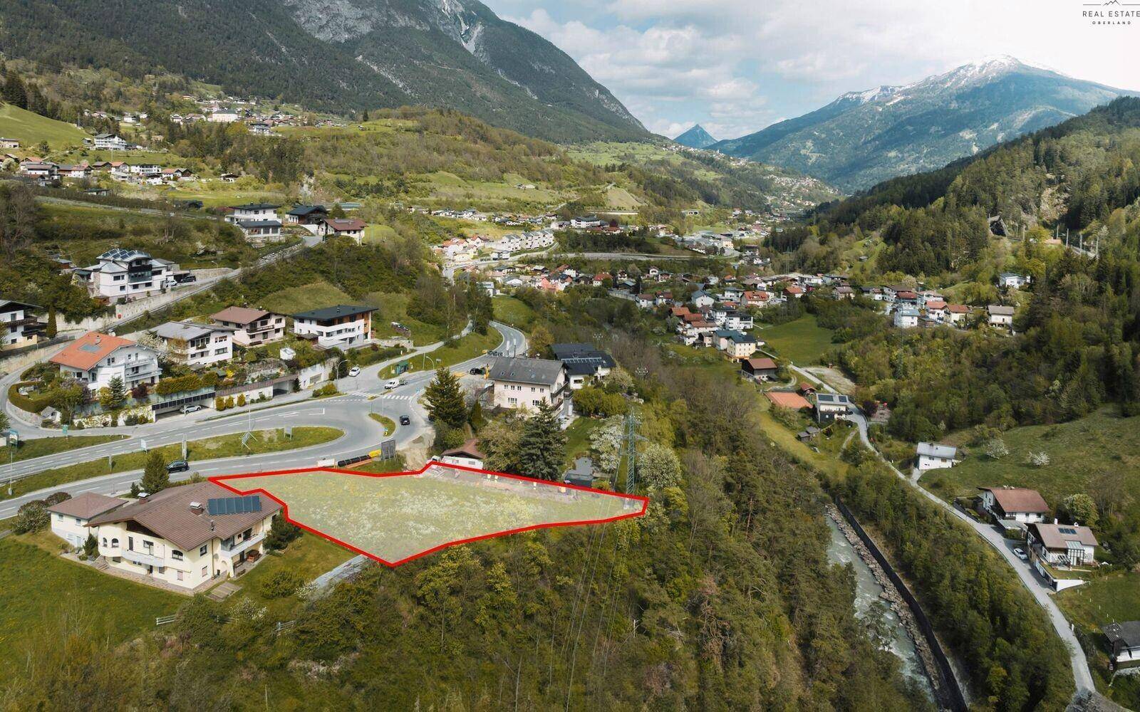Weitläufige Luftaufnahme eines Grundstücks in einem Tal, umgeben von bewaldeten Bergen und einer Siedlung.