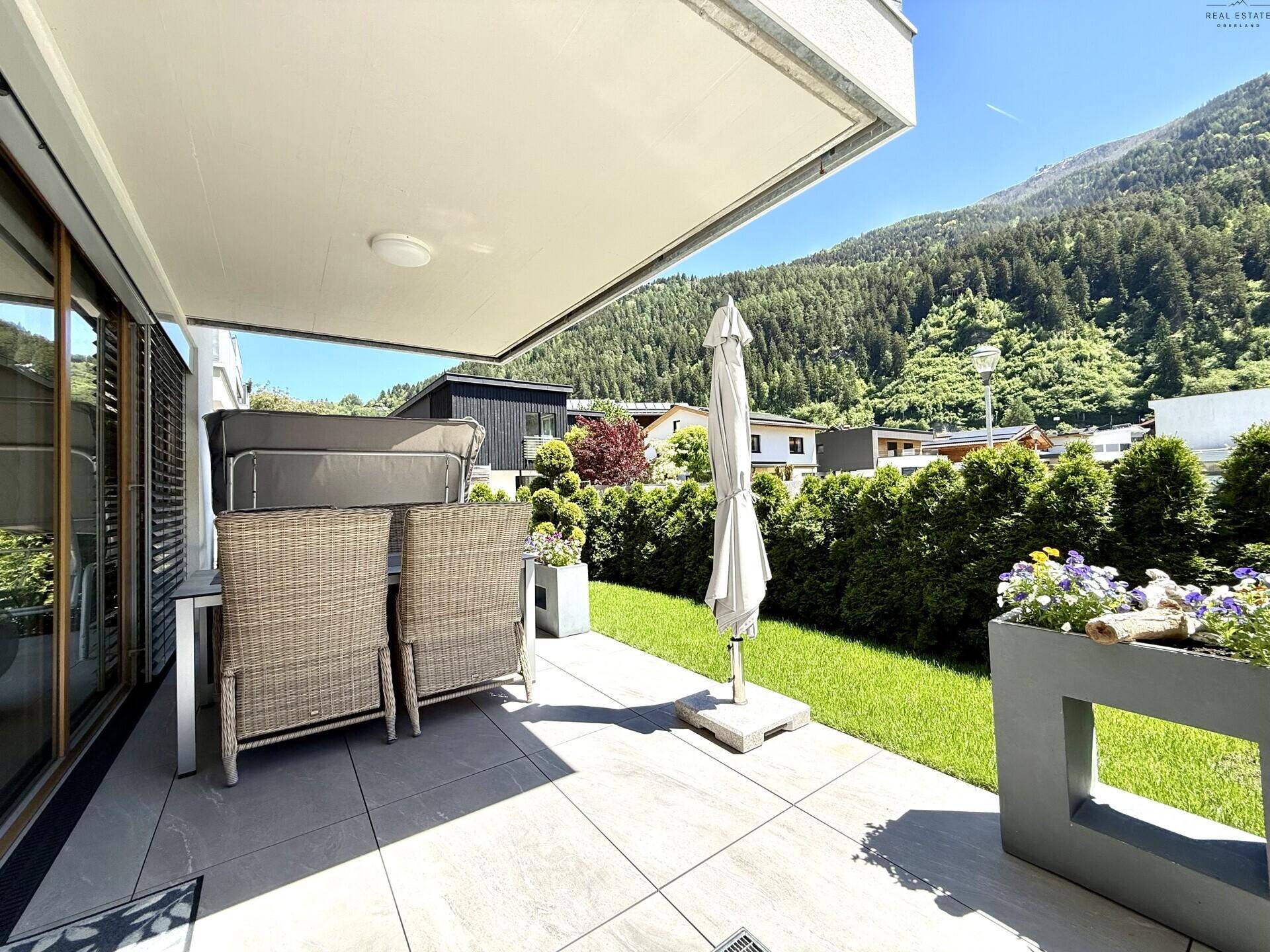Helle Terrasse mit Sitzgelegenheiten, Sonnenschirm und Panoramablick auf die Berglandschaft.